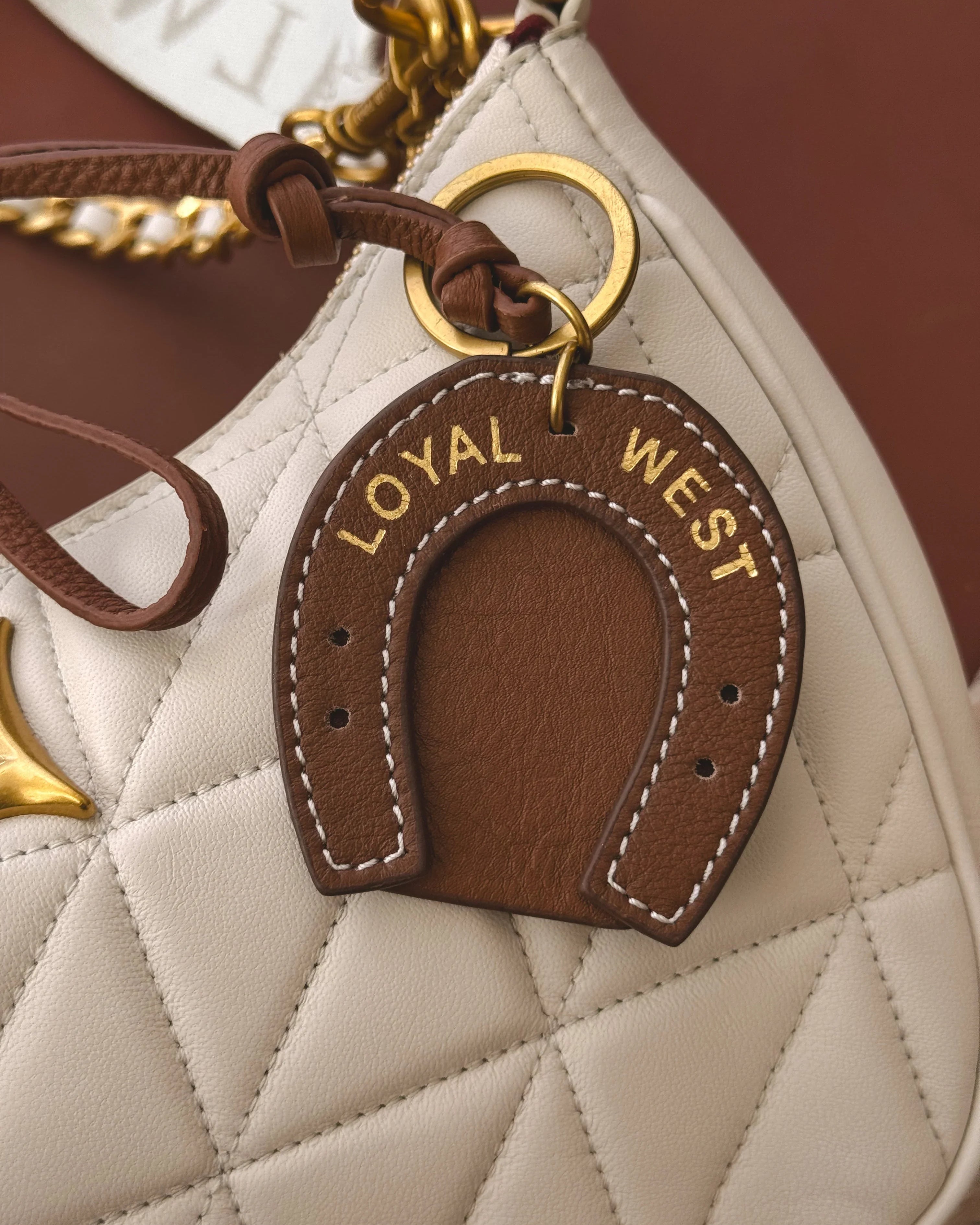 Horseshoe-shaped keychain with 'LOYAL WEST' text on a quilted handbag.