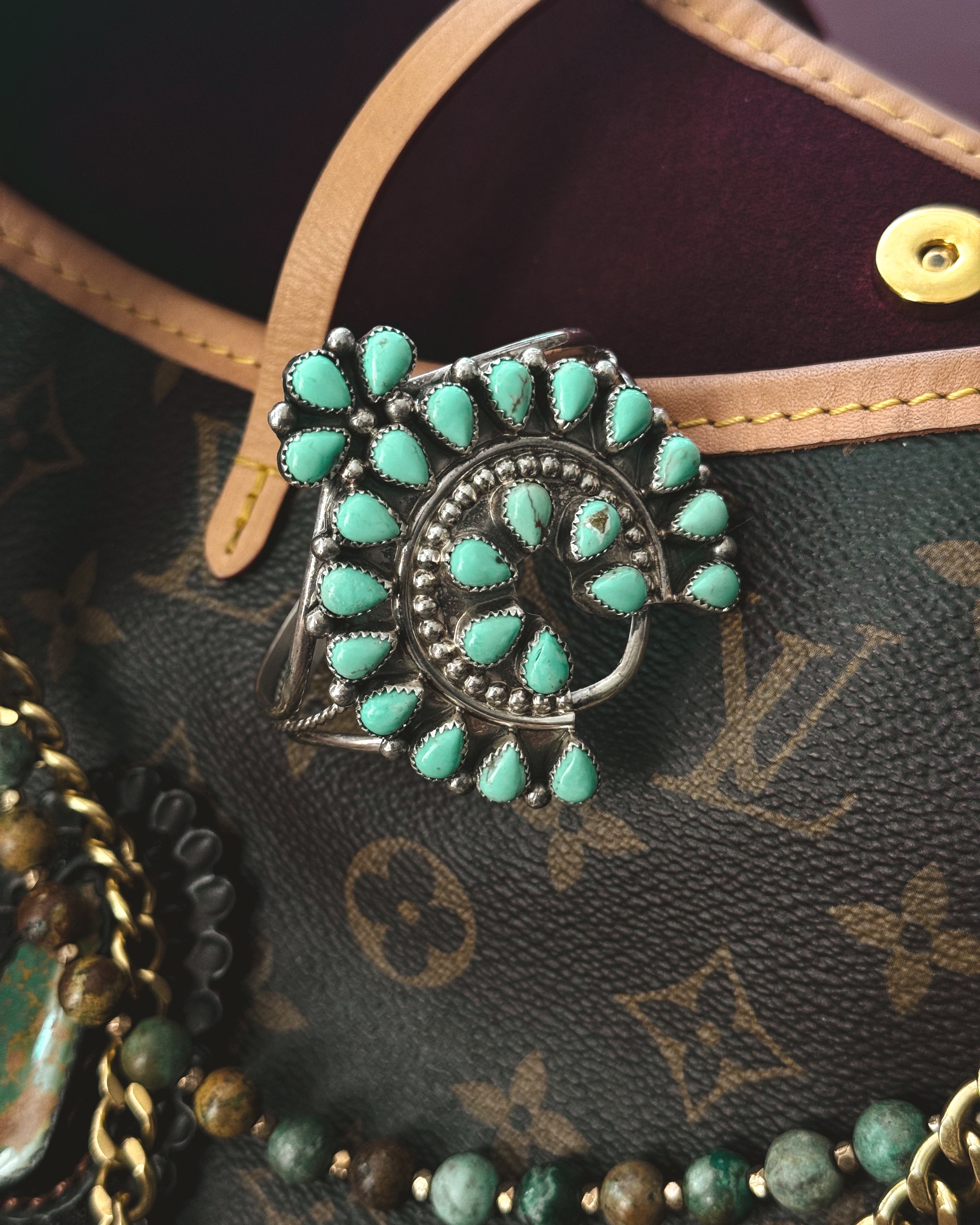 Turquoise western statement ring with silver setting on a leather designer bag surrounded by beaded jewelry.