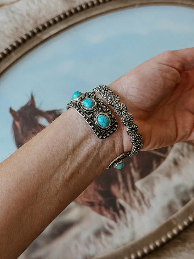 Hand wearing a silver bracelet with turquoise stones against a background of a horse painting.