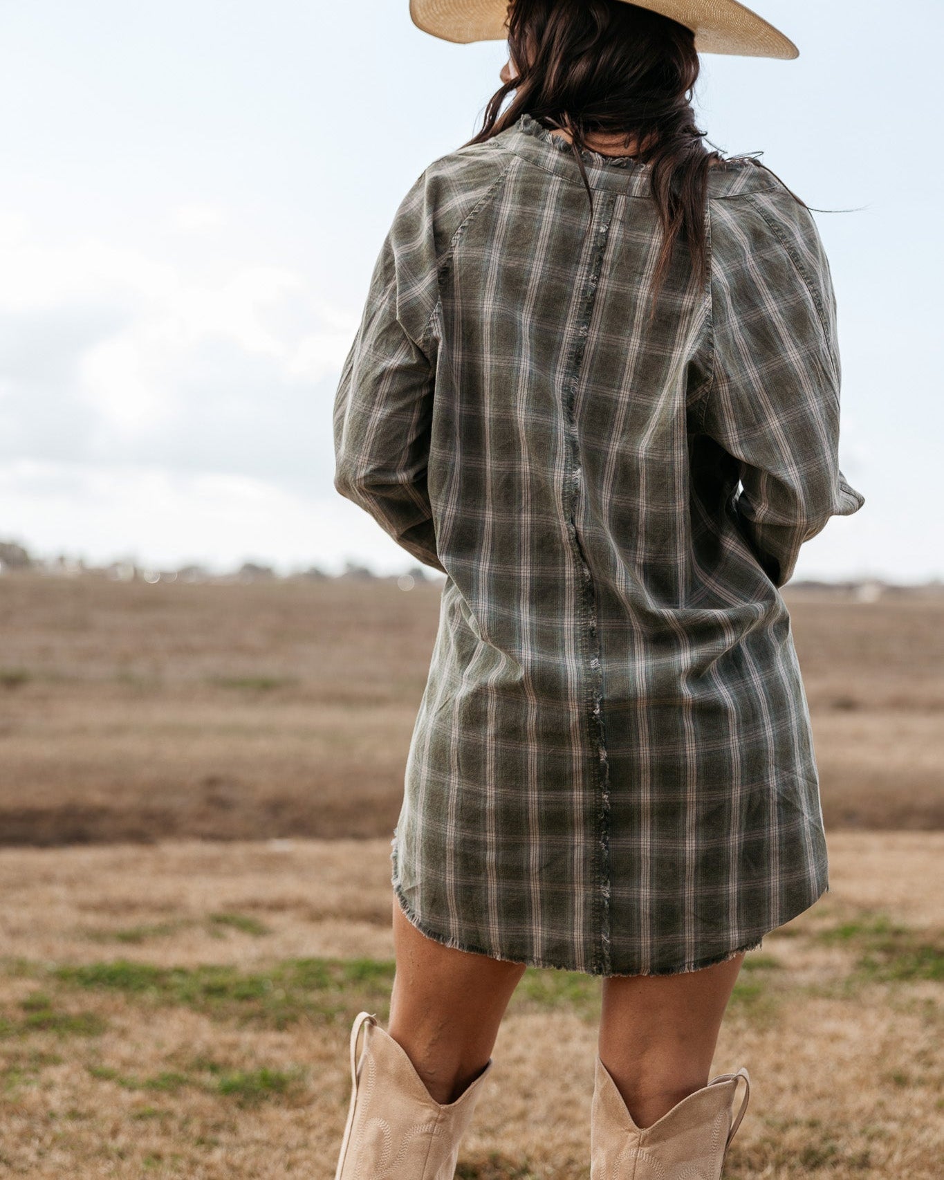 Woman in plaid western dress, cowboy boots, and cowboy hat standing outdoors
