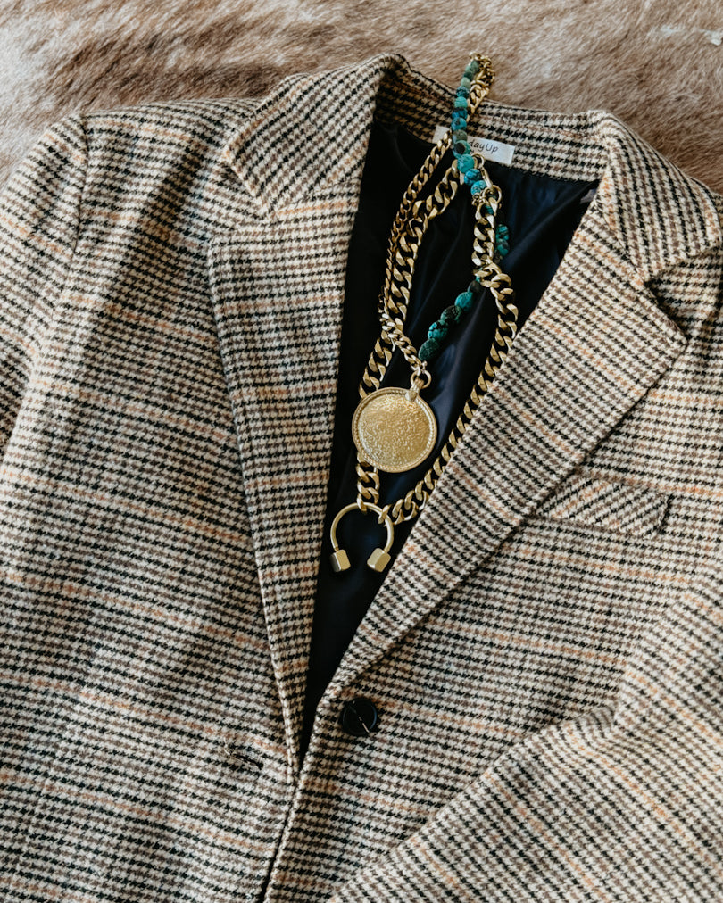 Plaid blazer with gold chain necklace on a textured surface