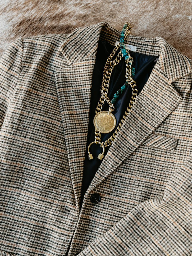 Plaid blazer with gold chain necklace on a textured surface