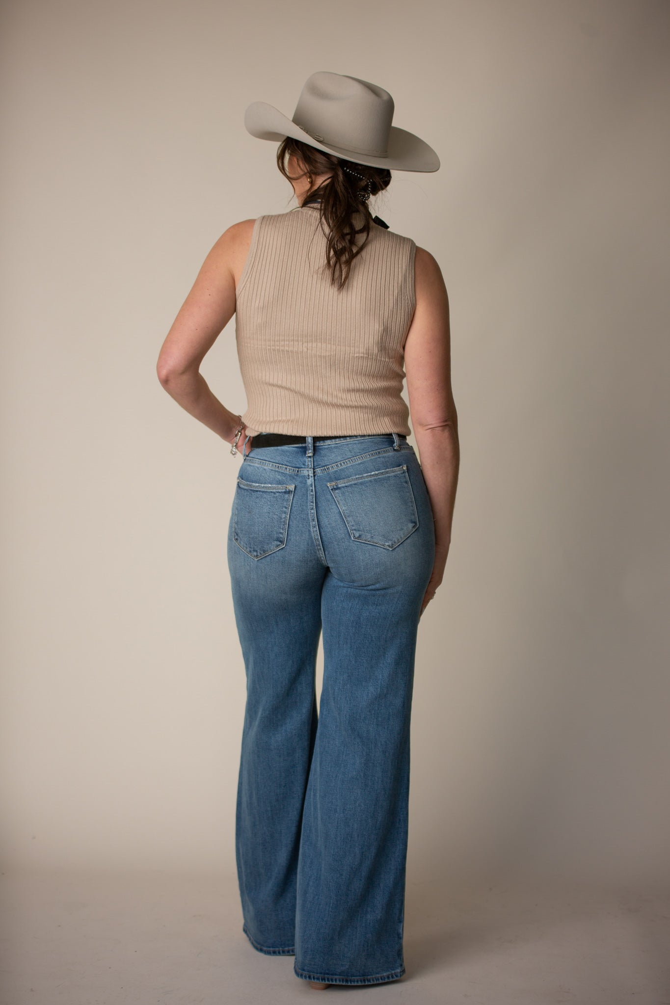 Woman in western outfit with wide-brim hat, sleeveless beige top, and flare blue jeans