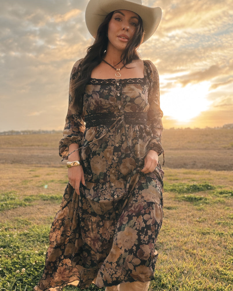 Woman in a floral western boho dress and cowboy hat at sunset in a field