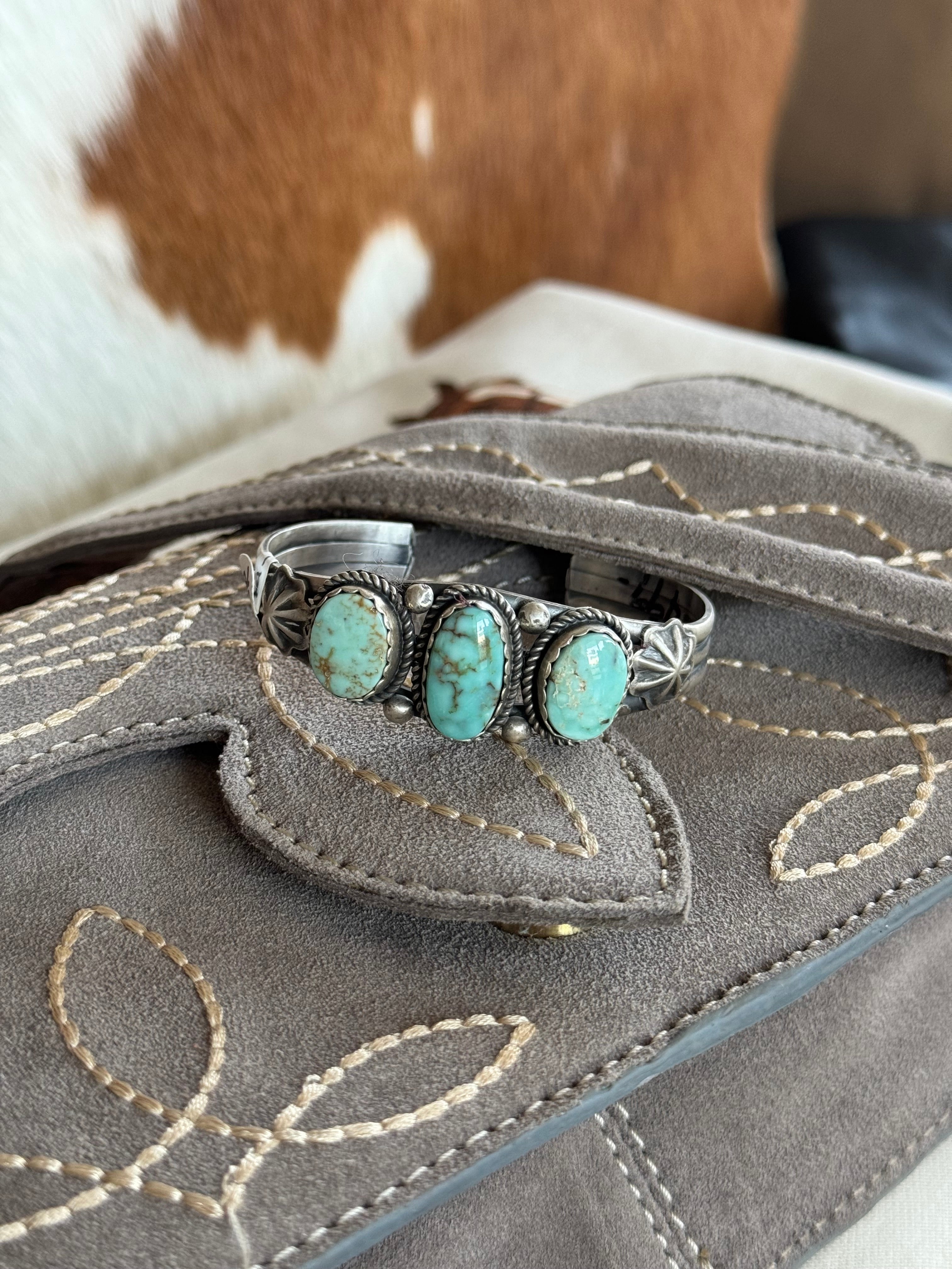 Western turquoise silver cuff bracelet on embroidered suede bag, cowhide backdrop