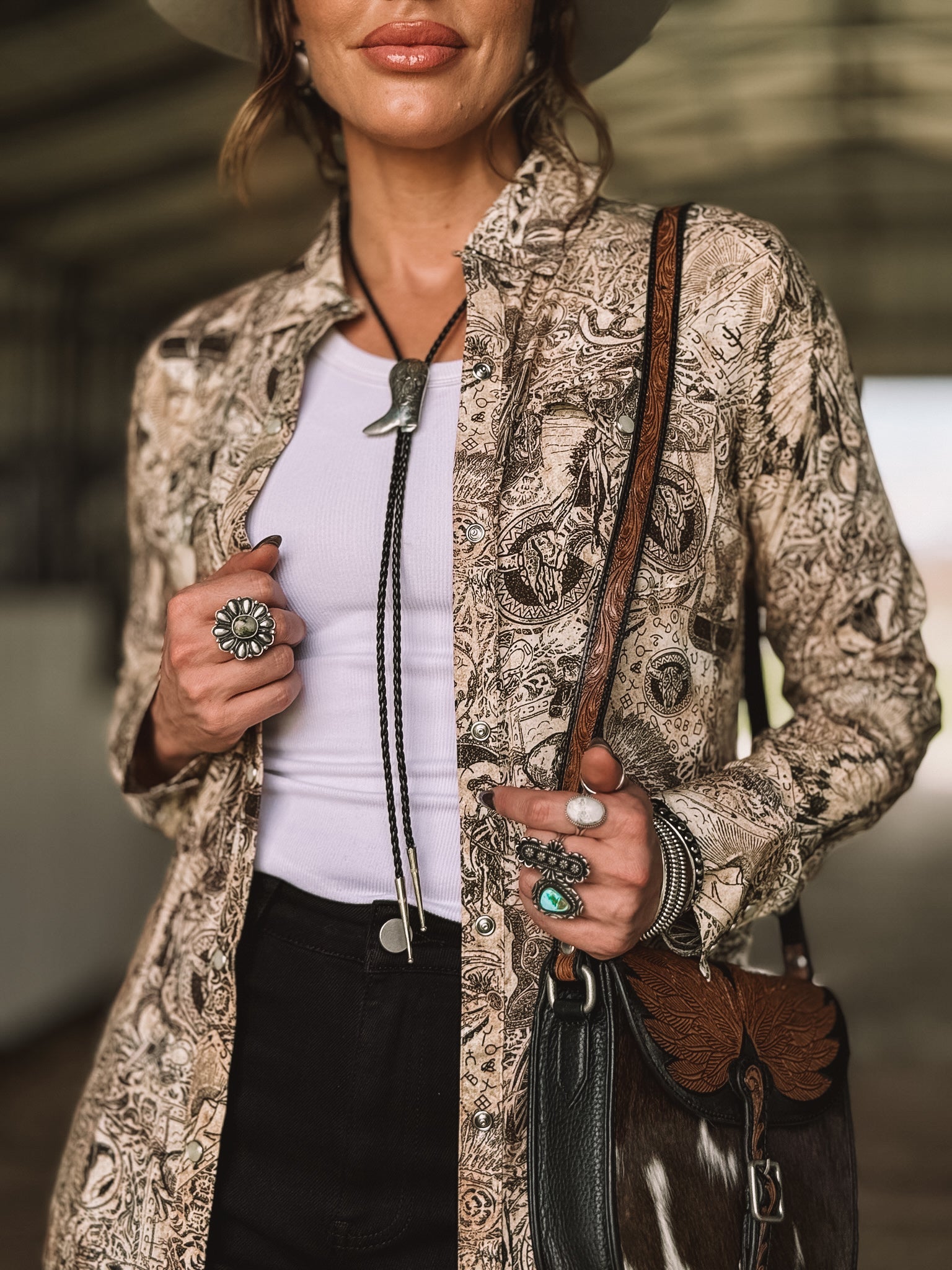 Woman in western boho shirt, bolo tie, silver rings, cowhide purse, and wide-brim hat