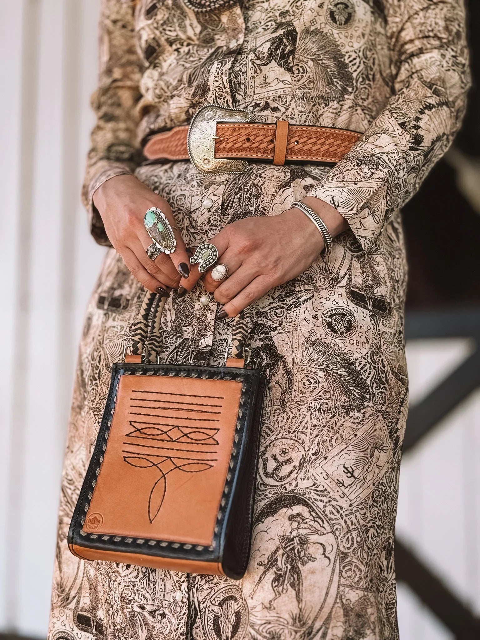 Woman in western print dress, tooled leather belt, statement rings, and tooled leather purse