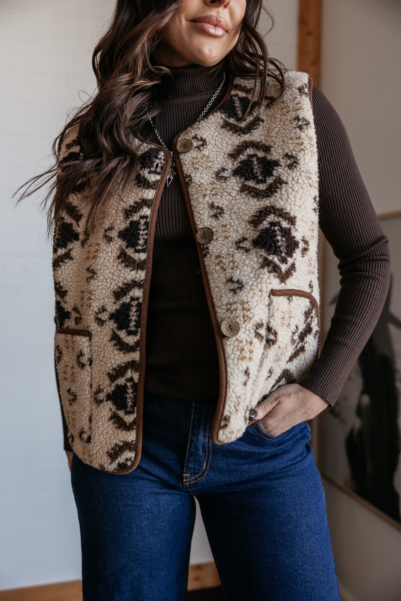 Woman wearing a western boho sherpa vest with tribal print, brown turtleneck, and blue jeans