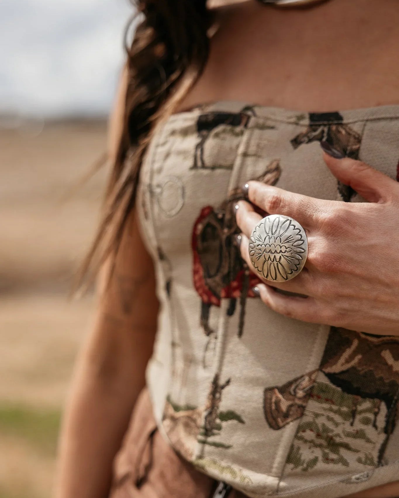 Woman wearing a western boho print corset top, statement silver ring, and brown suede pants