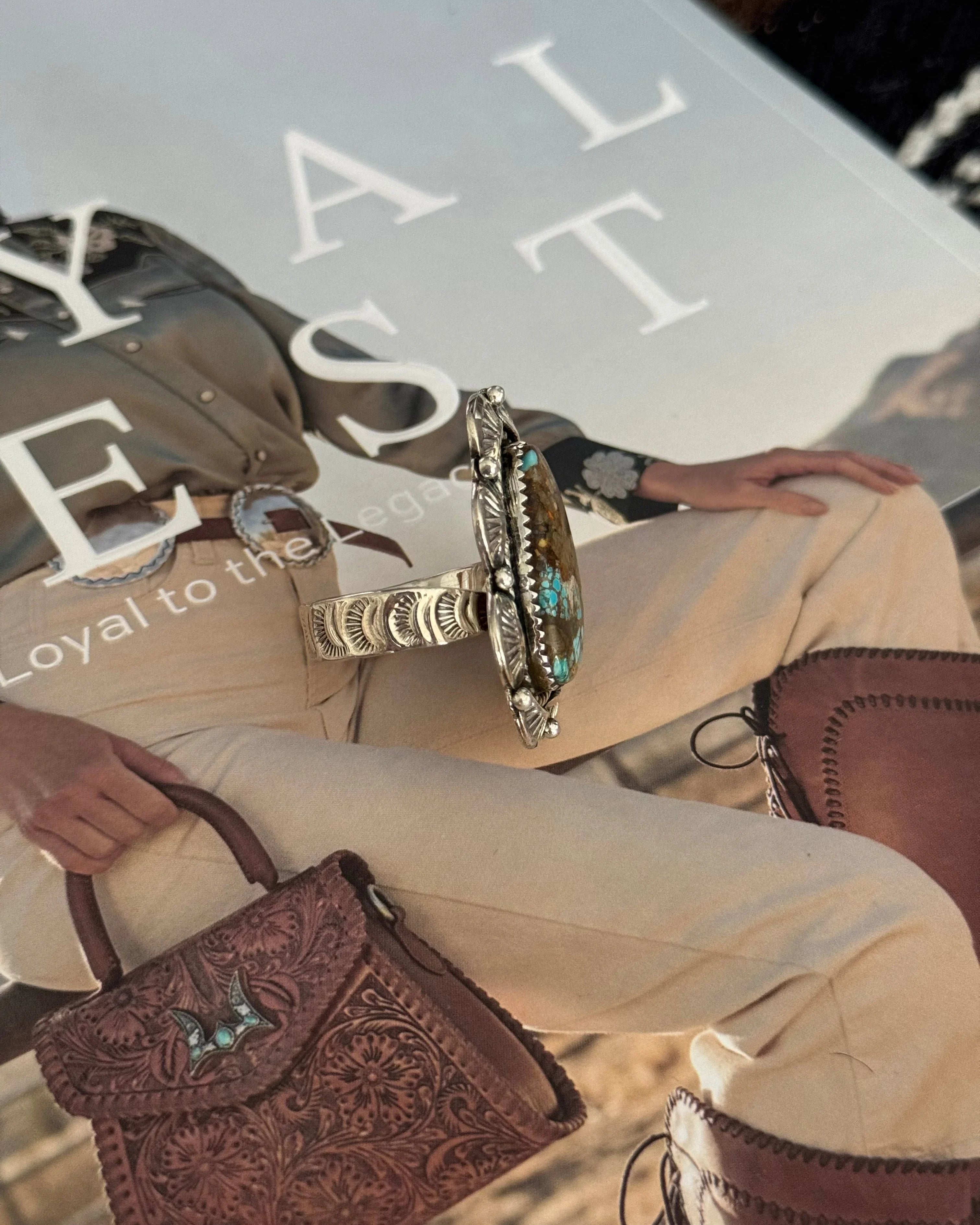 Western boho turquoise silver ring on embossed leather bag and cowgirl outfit background