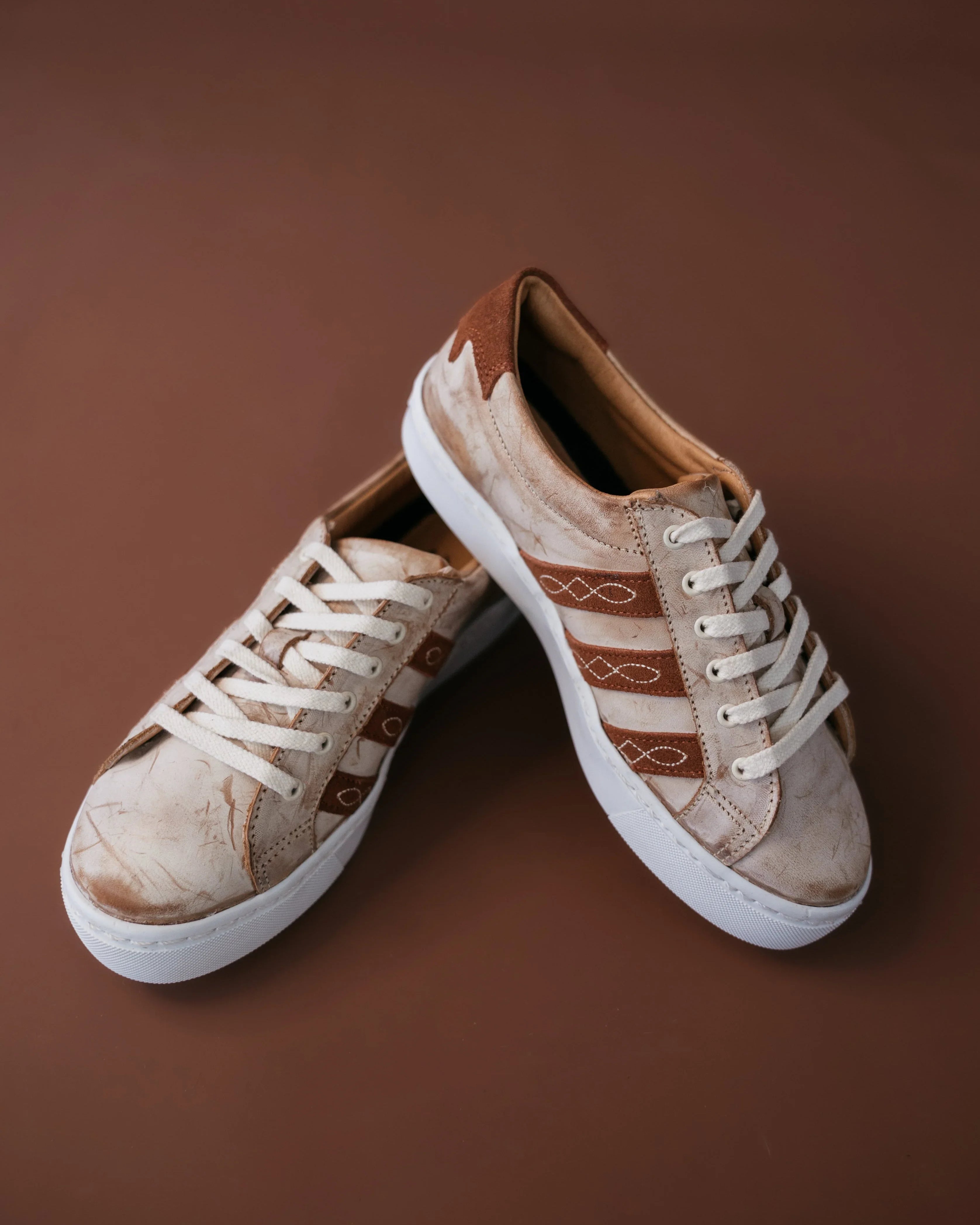 Western-inspired brown and tan sneakers with white laces on brown background