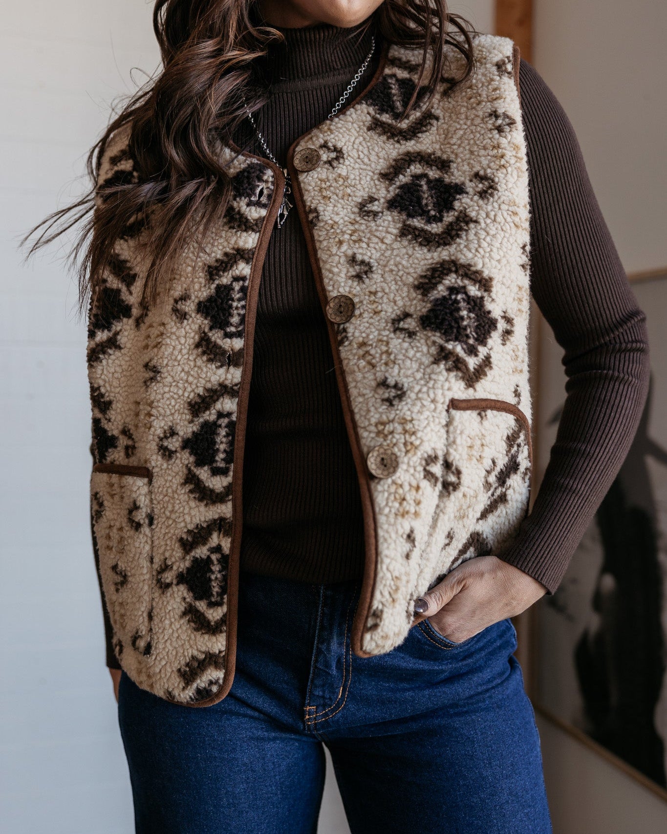 Woman wearing western sherpa vest with aztec pattern, brown turtleneck, and denim jeans