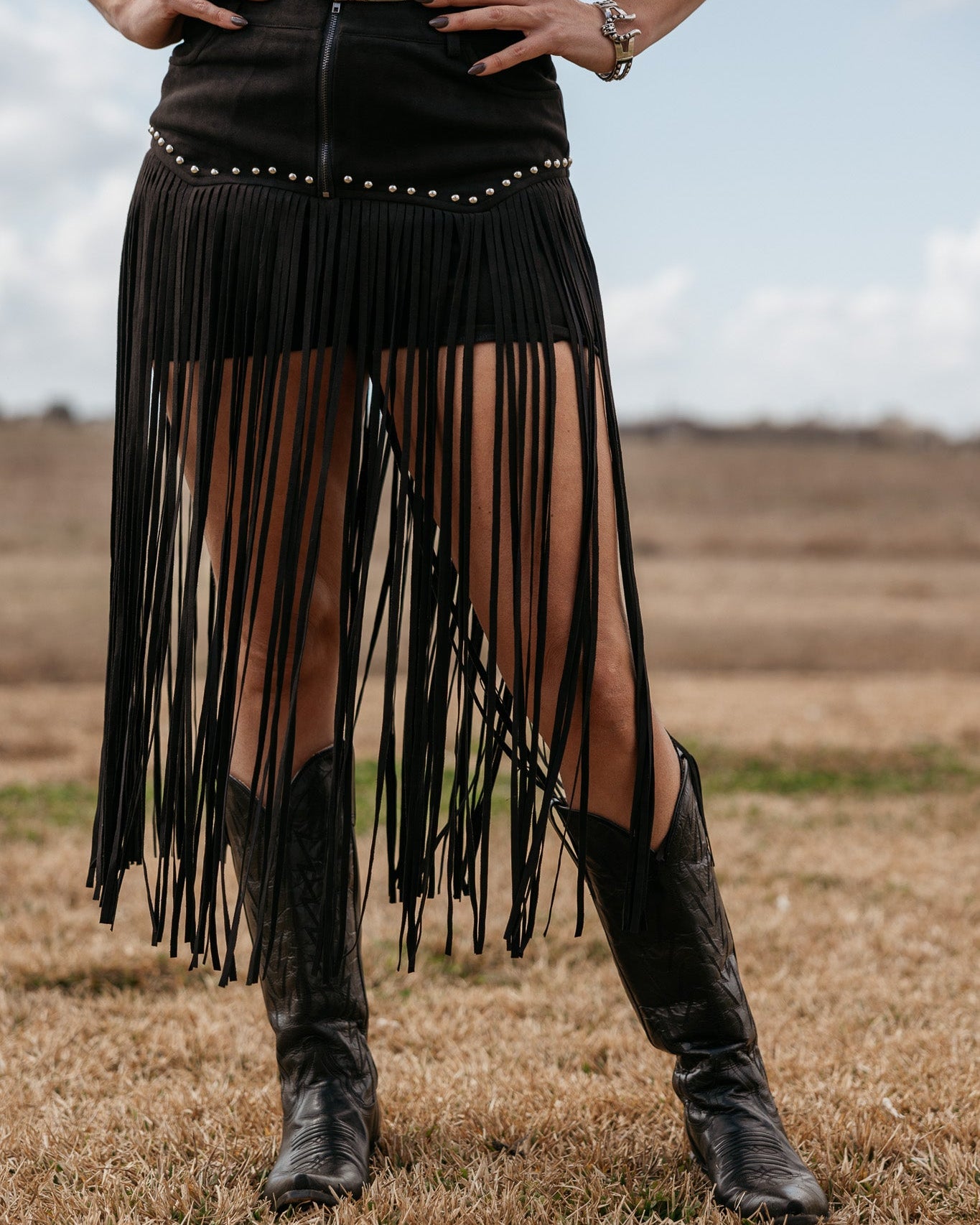 Woman wearing black fringe western skirt and cowboy boots in a country field