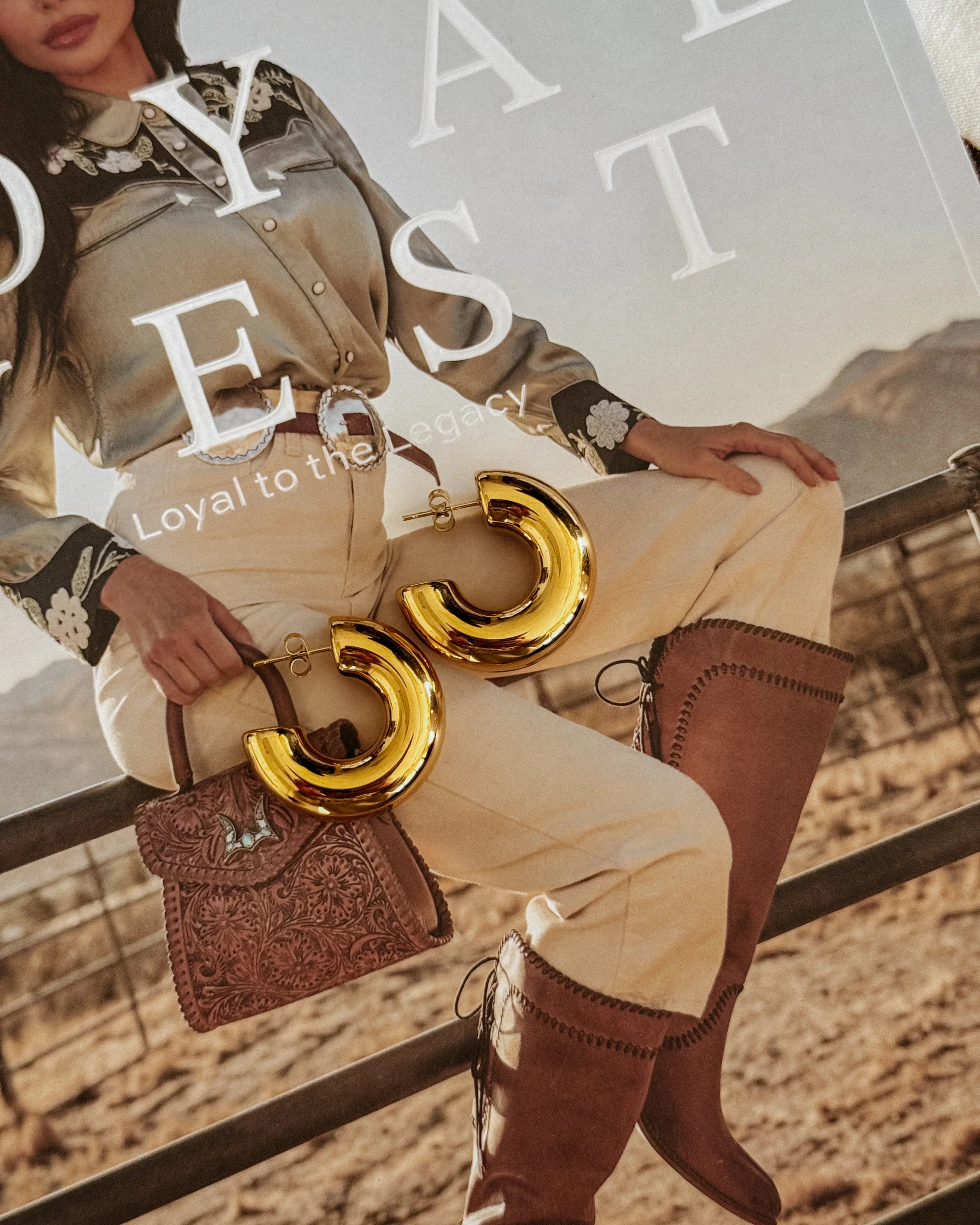 Gold western hoop earrings on cowgirl fashion magazine with boots, tooled purse and rodeo outfit.