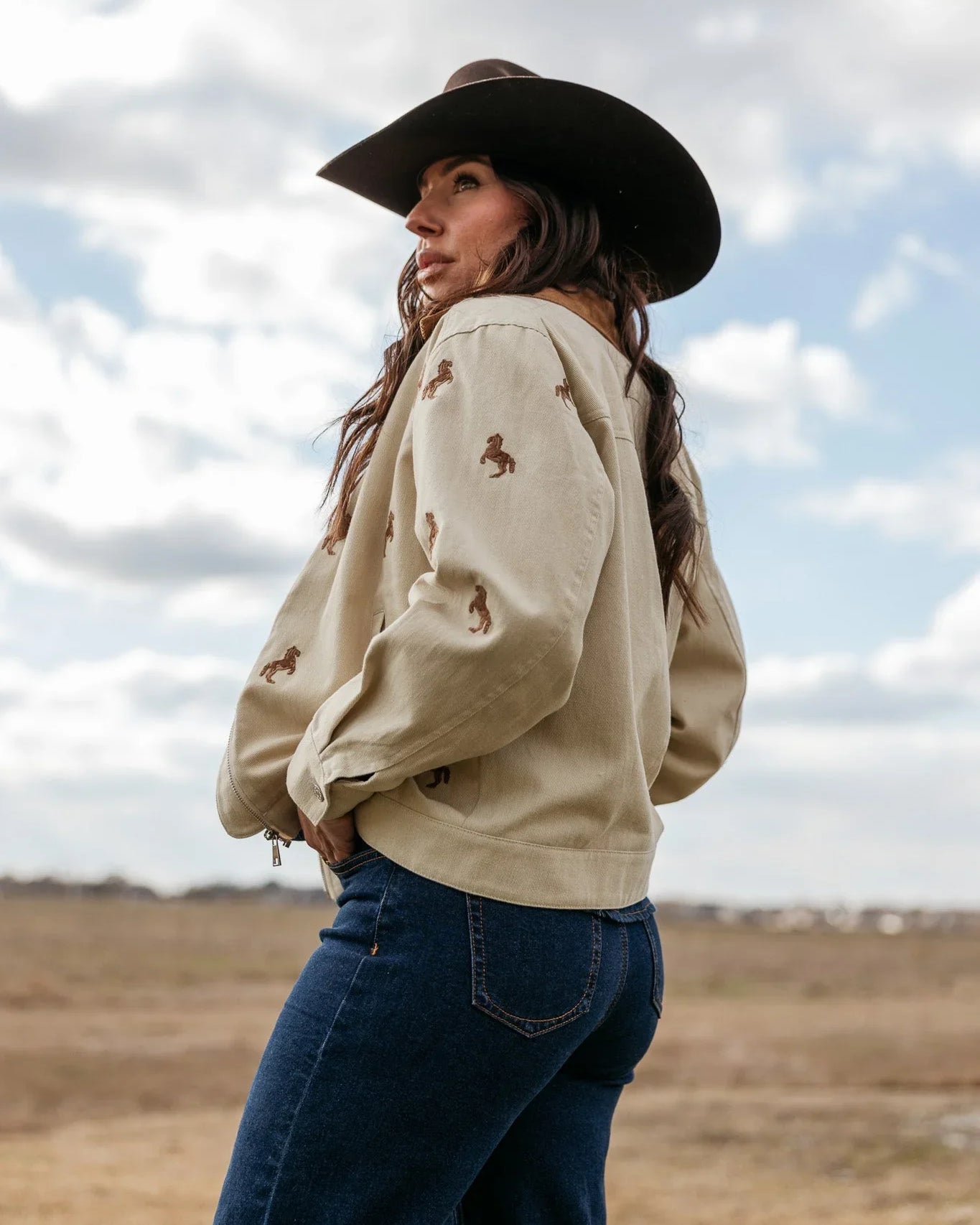 Woman in cowgirl hat, beige embroidered western jacket and blue jeans outdoors