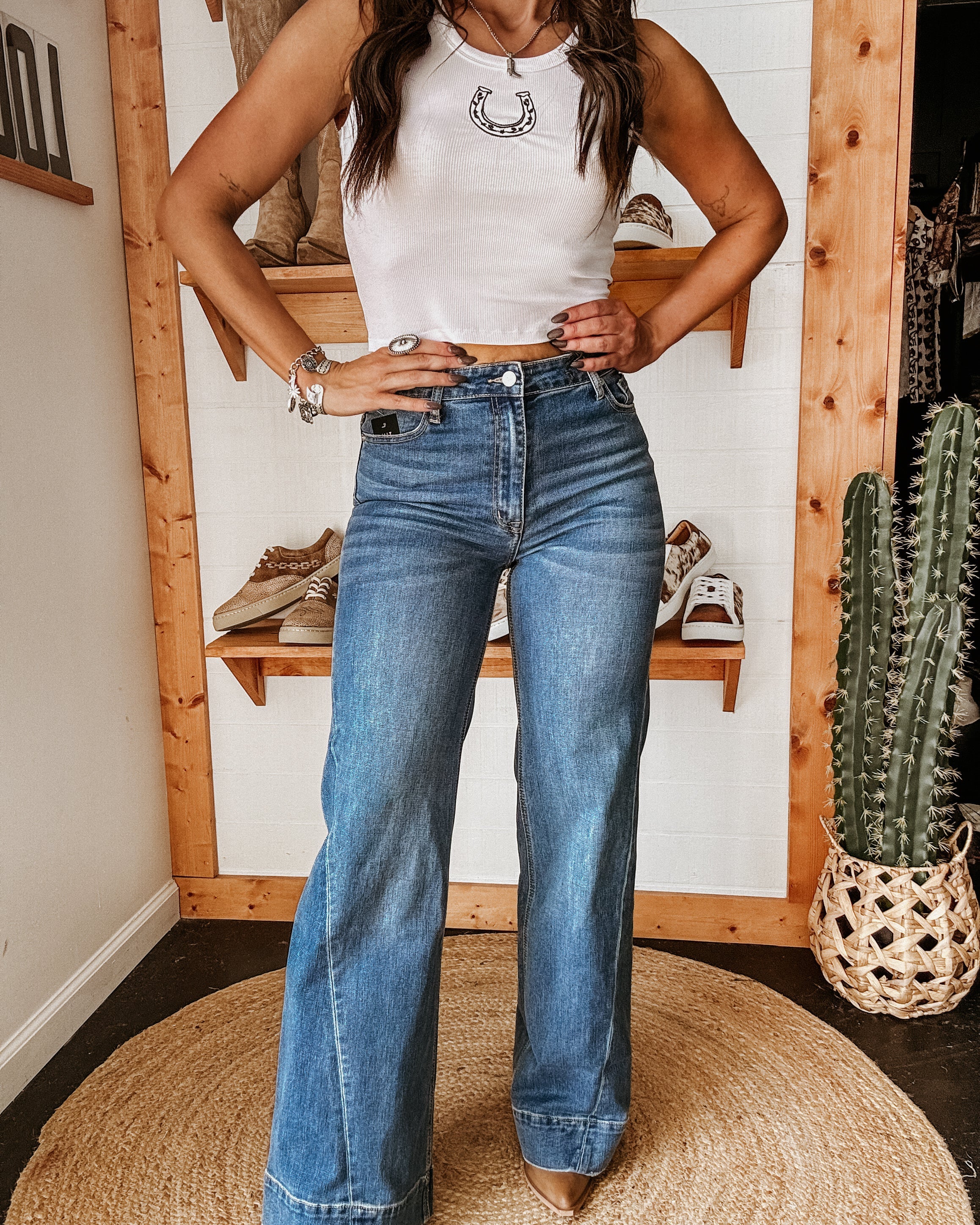Woman wearing a white crop top with horseshoe graphic and high-waisted flare jeans in a western boutique setting.