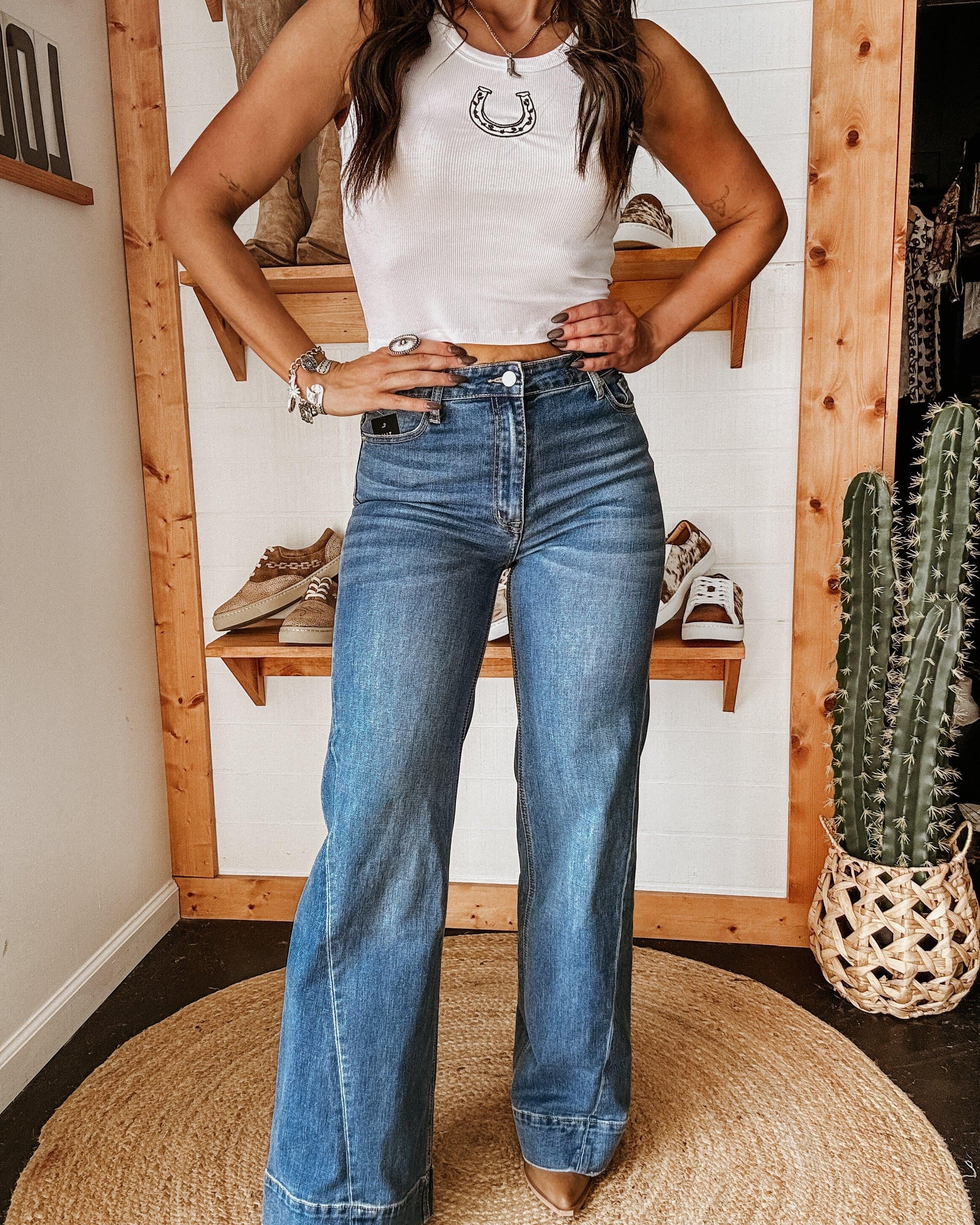 Woman wearing a white crop top with horseshoe graphic and high-waisted flare jeans in a western boutique setting.