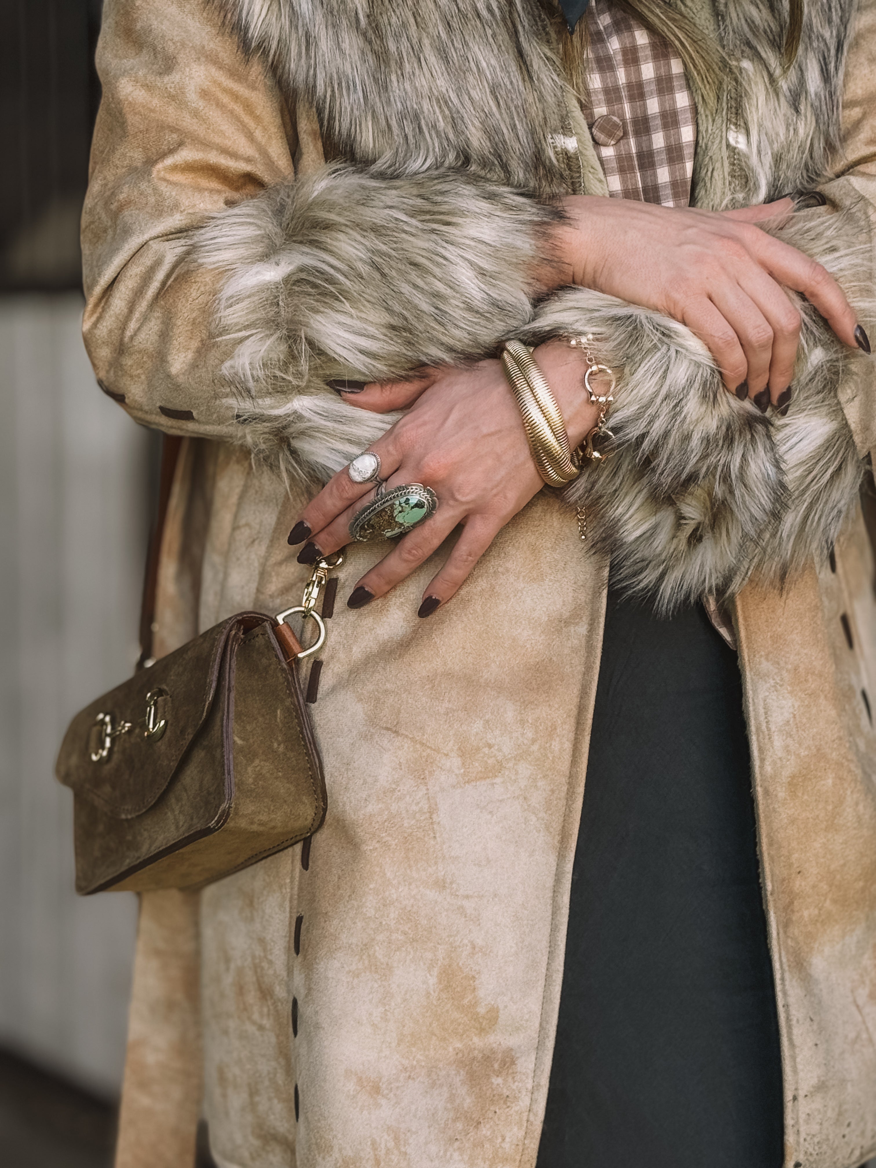Woman in faux fur western coat, plaid shirt, statement rings, and brown suede purse
