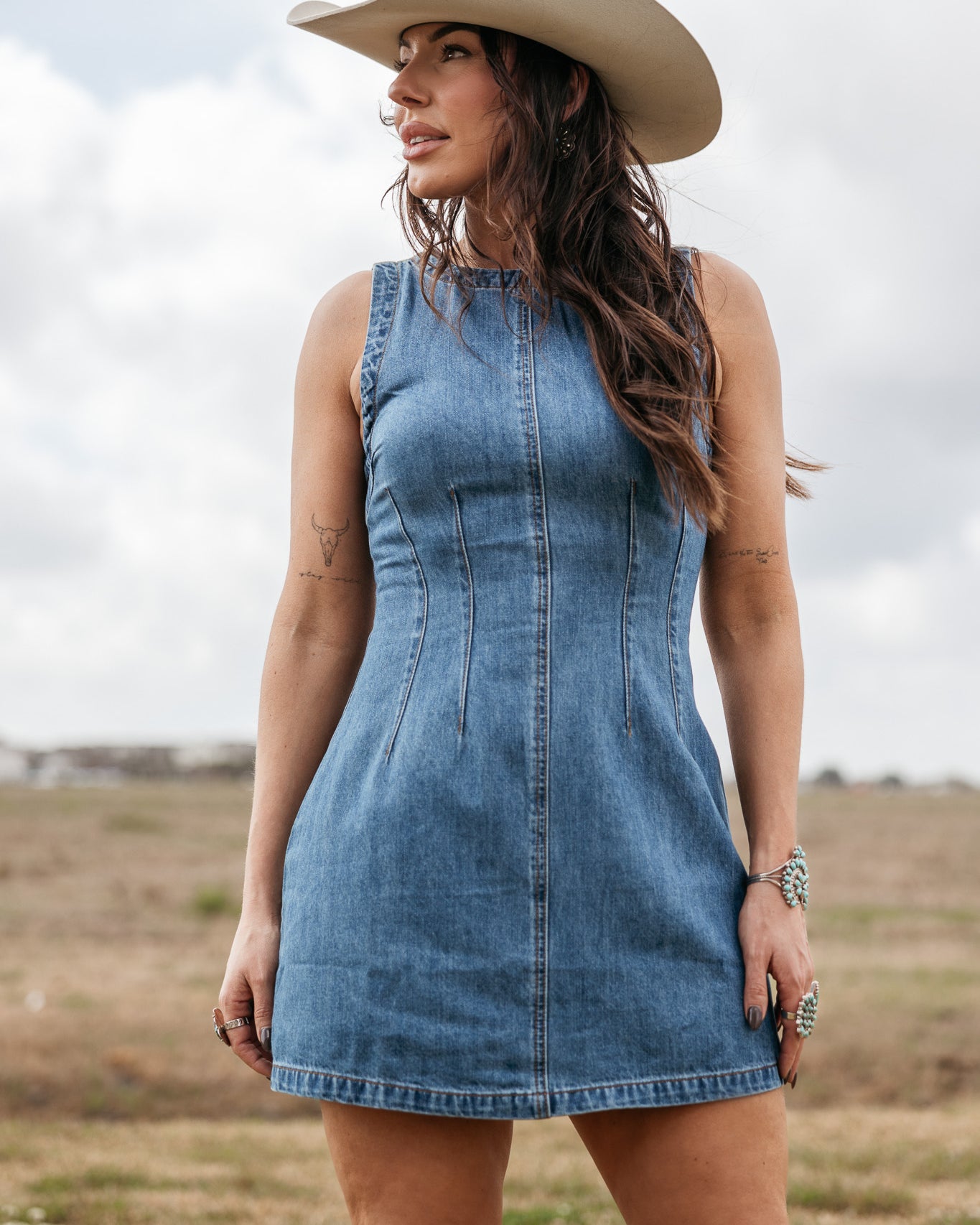 Woman in a denim western dress and cowboy hat standing outdoors in a field