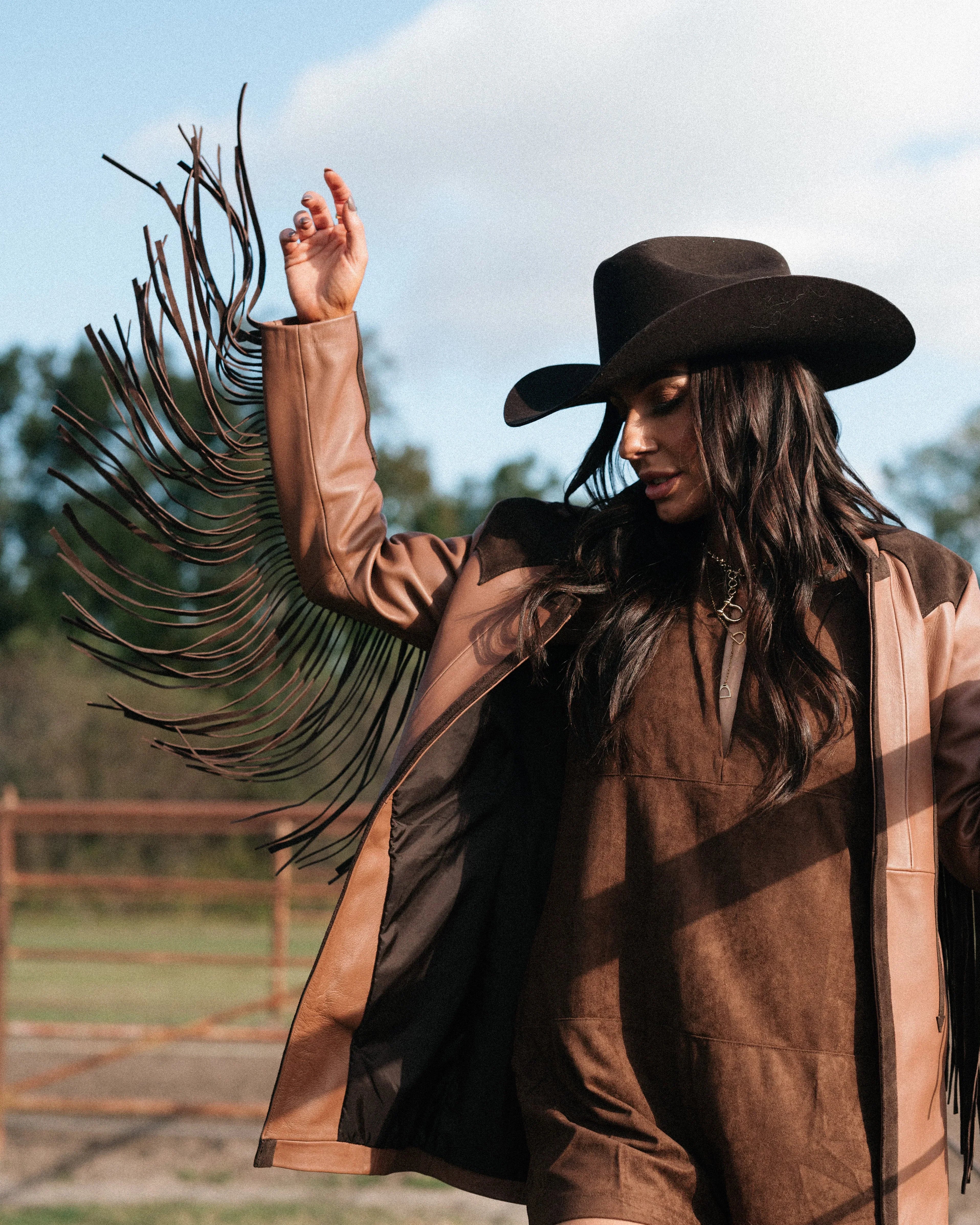 Woman in brown fringe western jacket and cowboy hat outdoors, boho cowgirl outfit