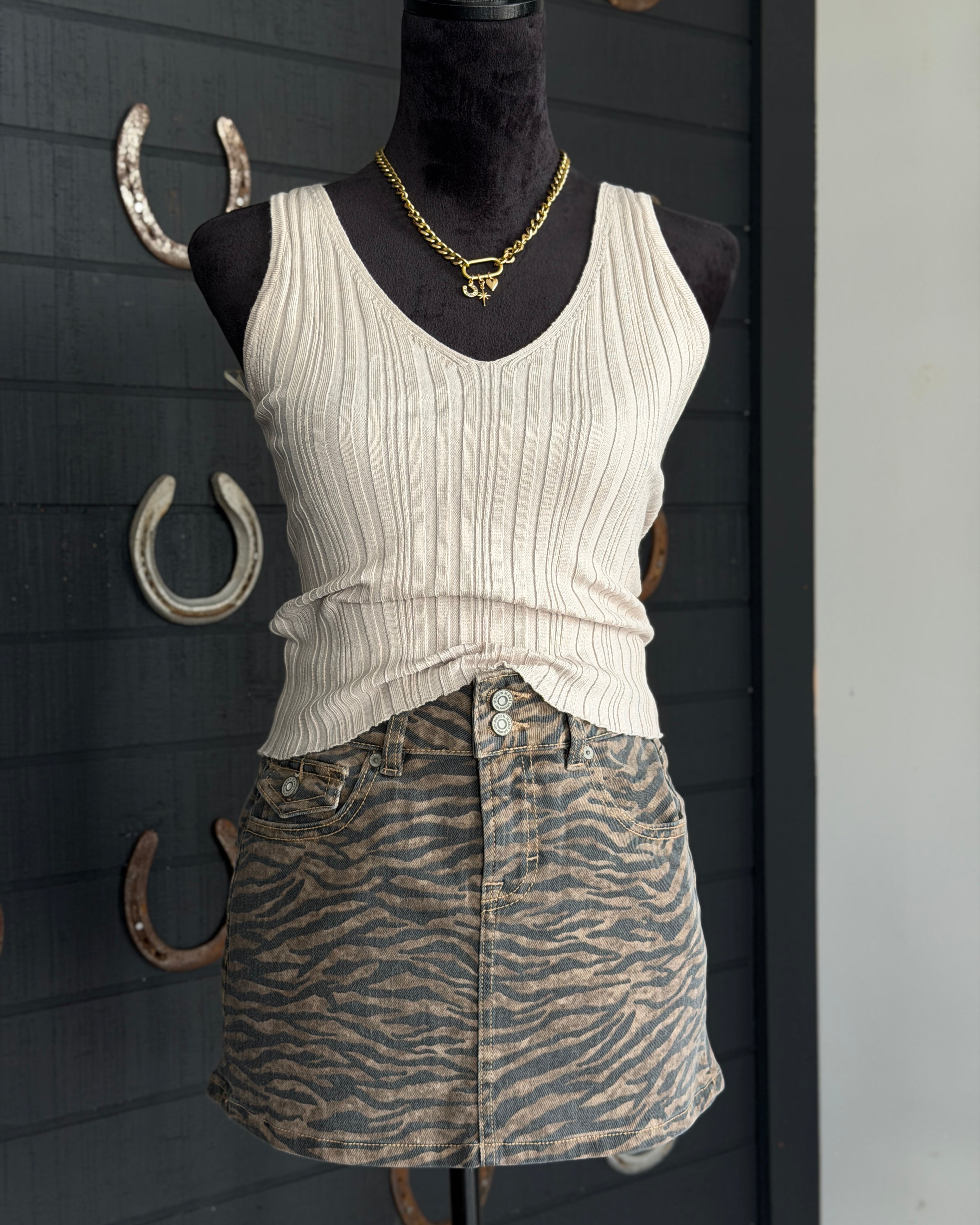 Mannequin wearing a white ribbed tank top and zebra print skirt against a dark background with horseshoes.
