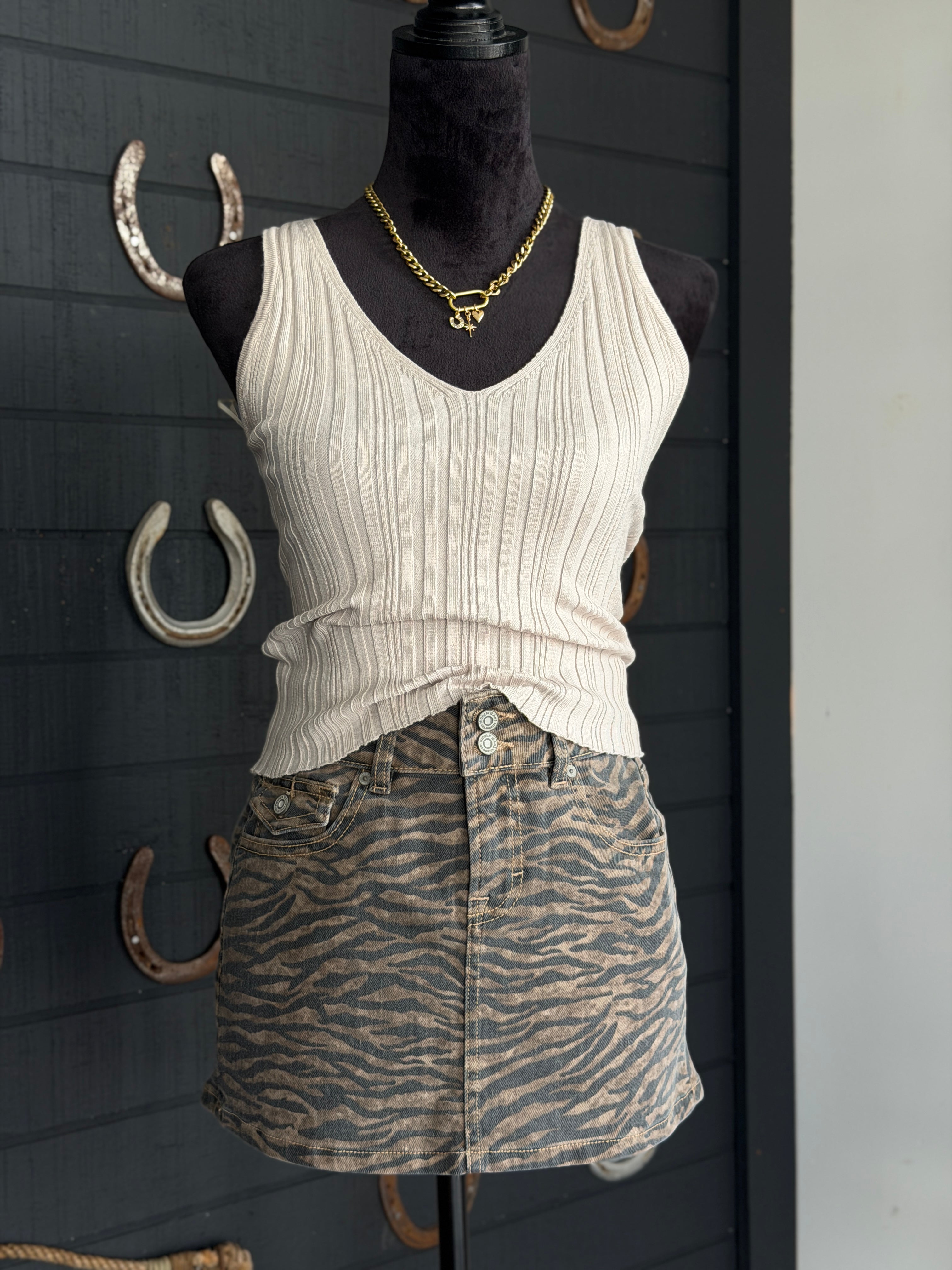 Mannequin wearing a white ribbed tank top and zebra print skirt against a dark background with horseshoes.
