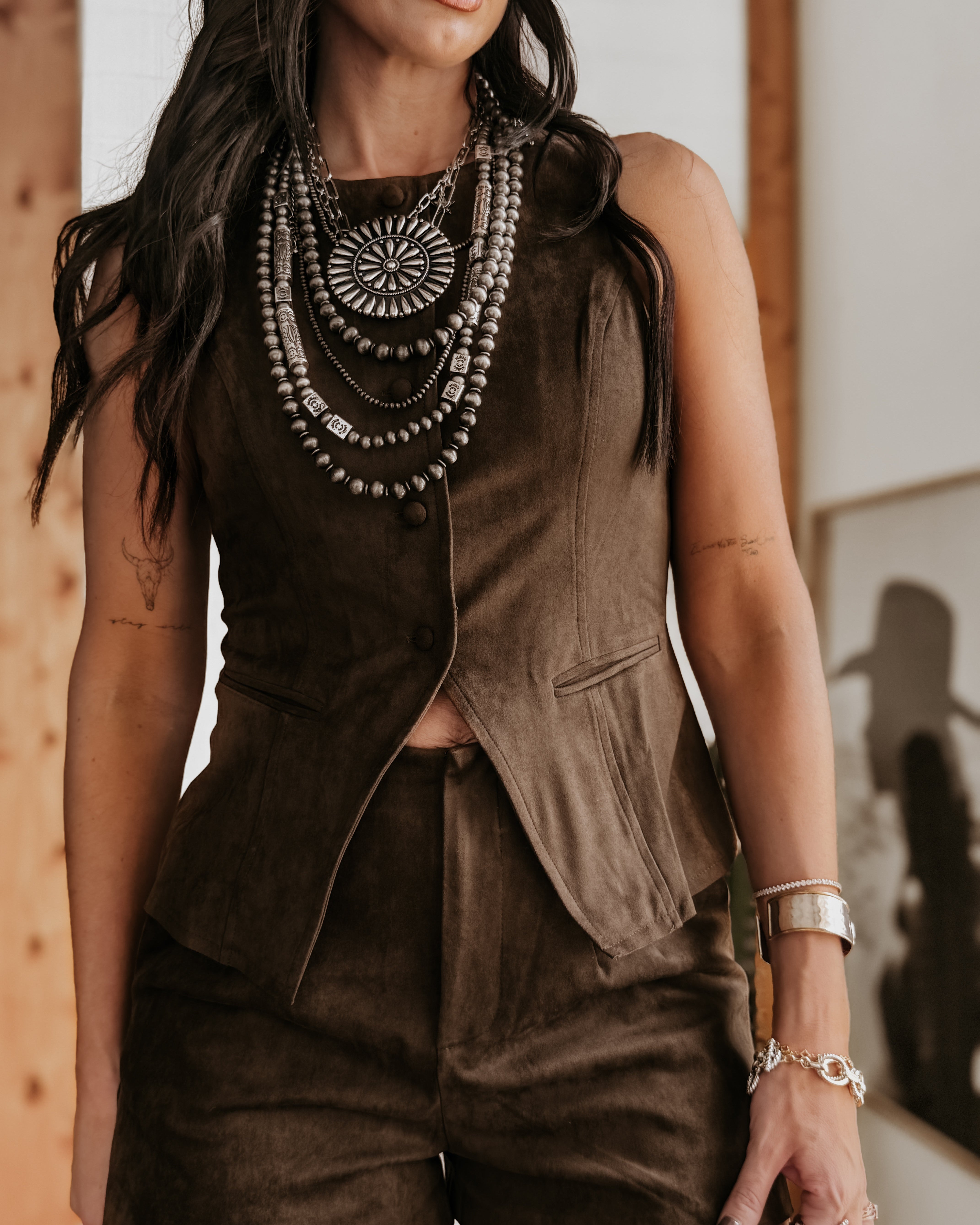 Woman wearing brown suede western vest and shorts set with layered silver boho necklaces.