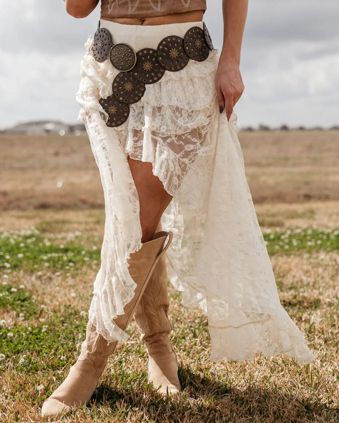 Woman in western lace skirt, concho belt, and tan cowboy boots outdoors