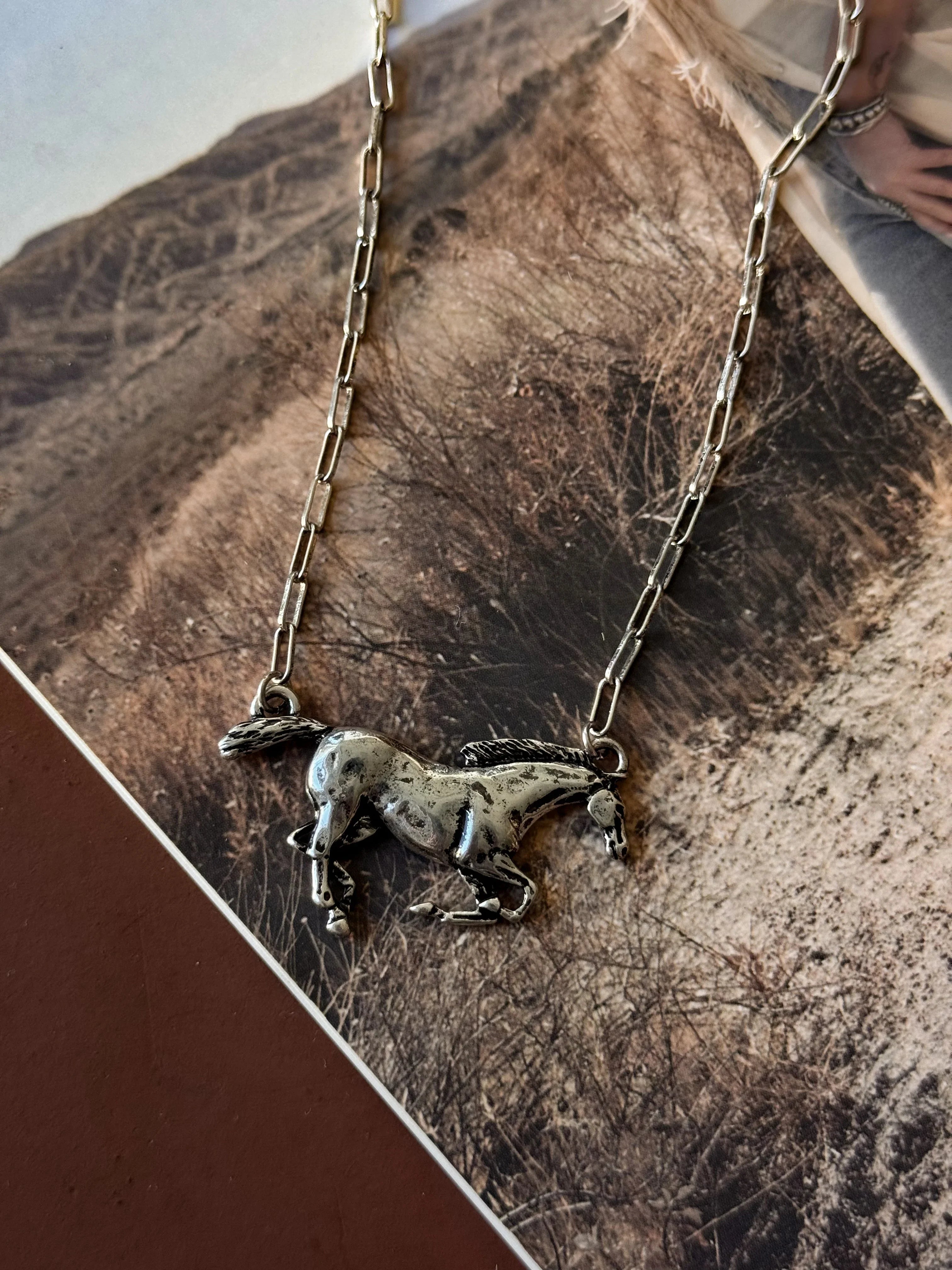 Silver horse pendant necklace on a textured surface