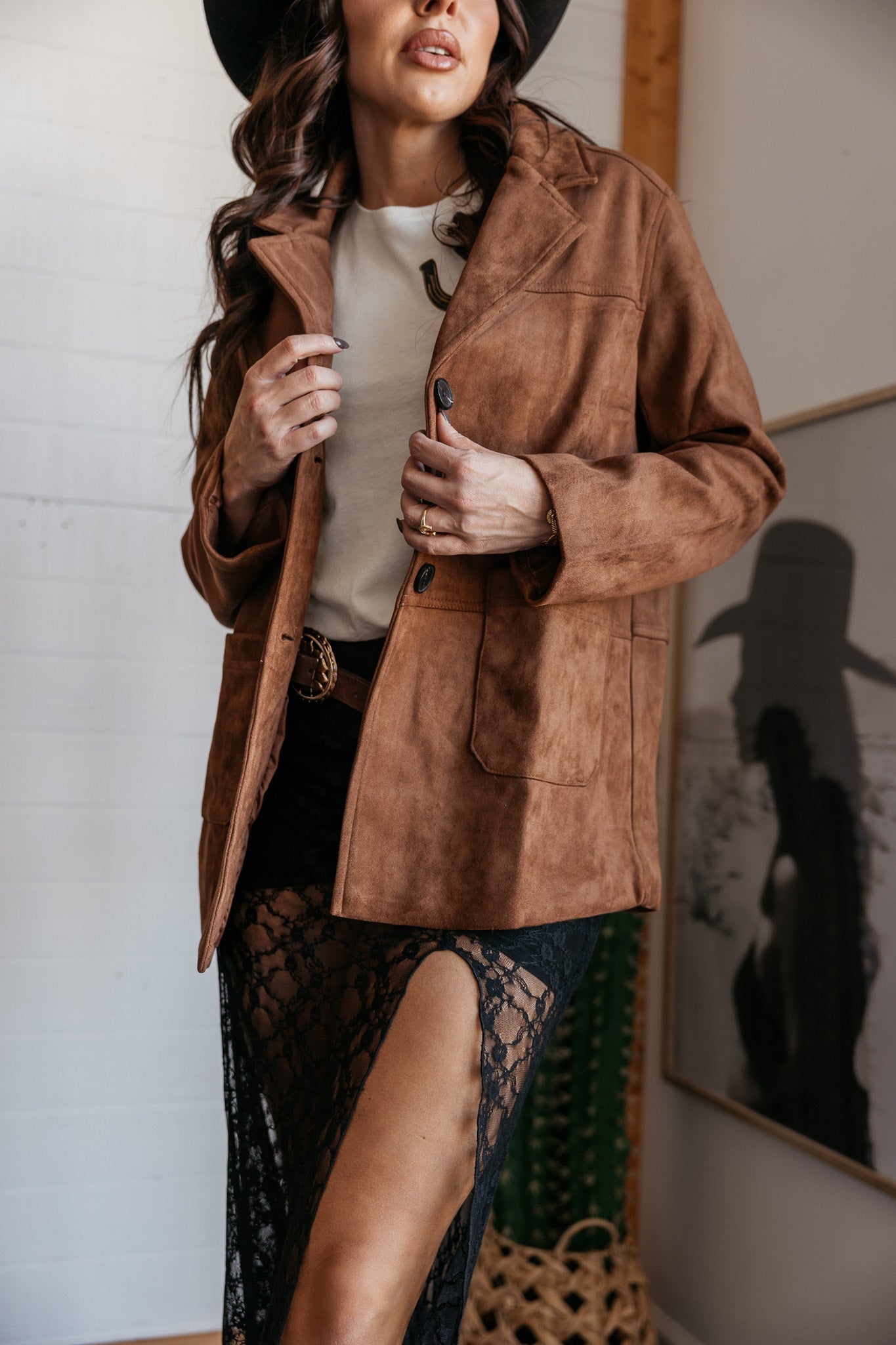 Woman in a brown suede western jacket, black lace skirt with thigh-high slit, and wide-brim hat