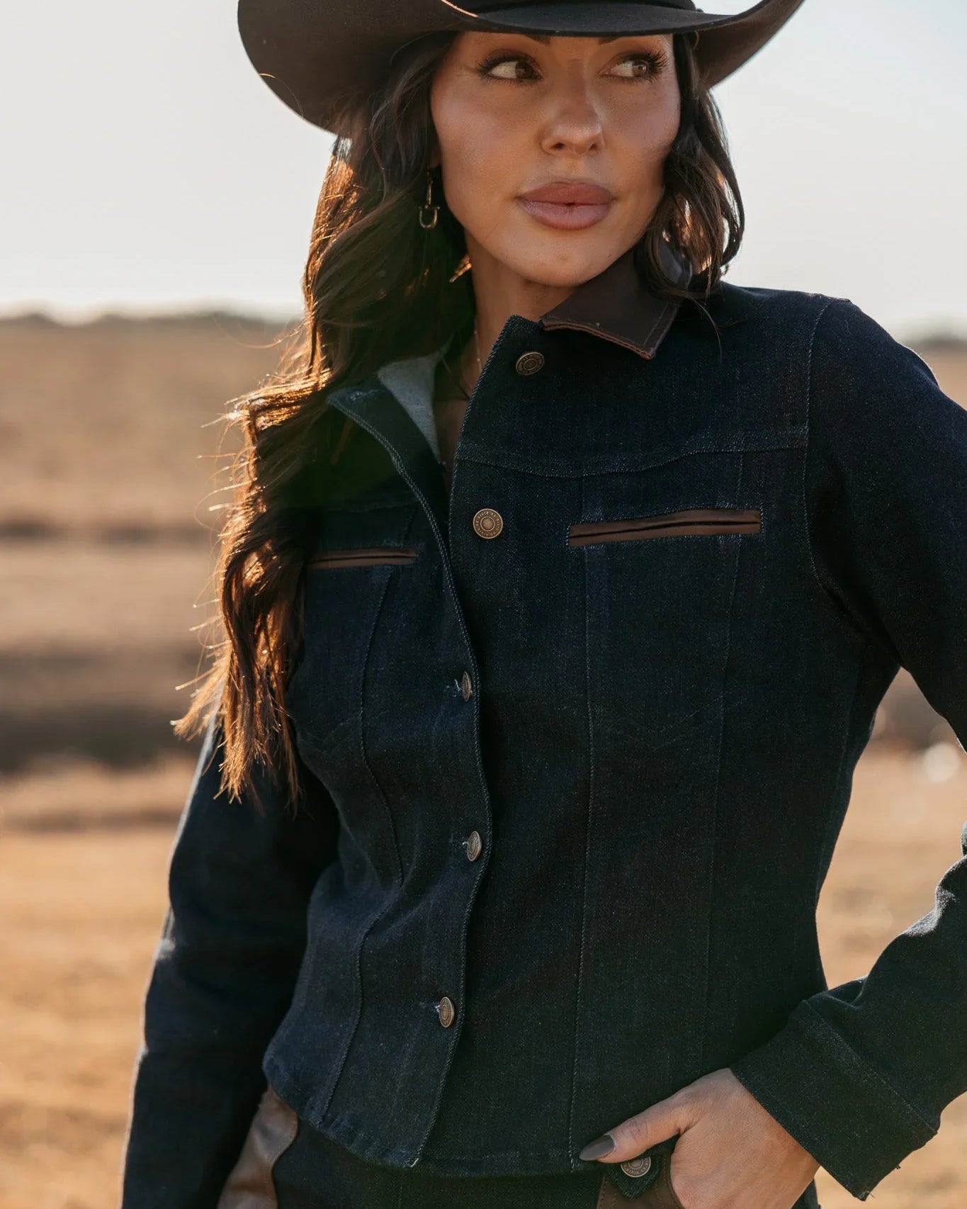 Woman in dark denim western jacket and cowboy hat outdoors, western boho fashion style