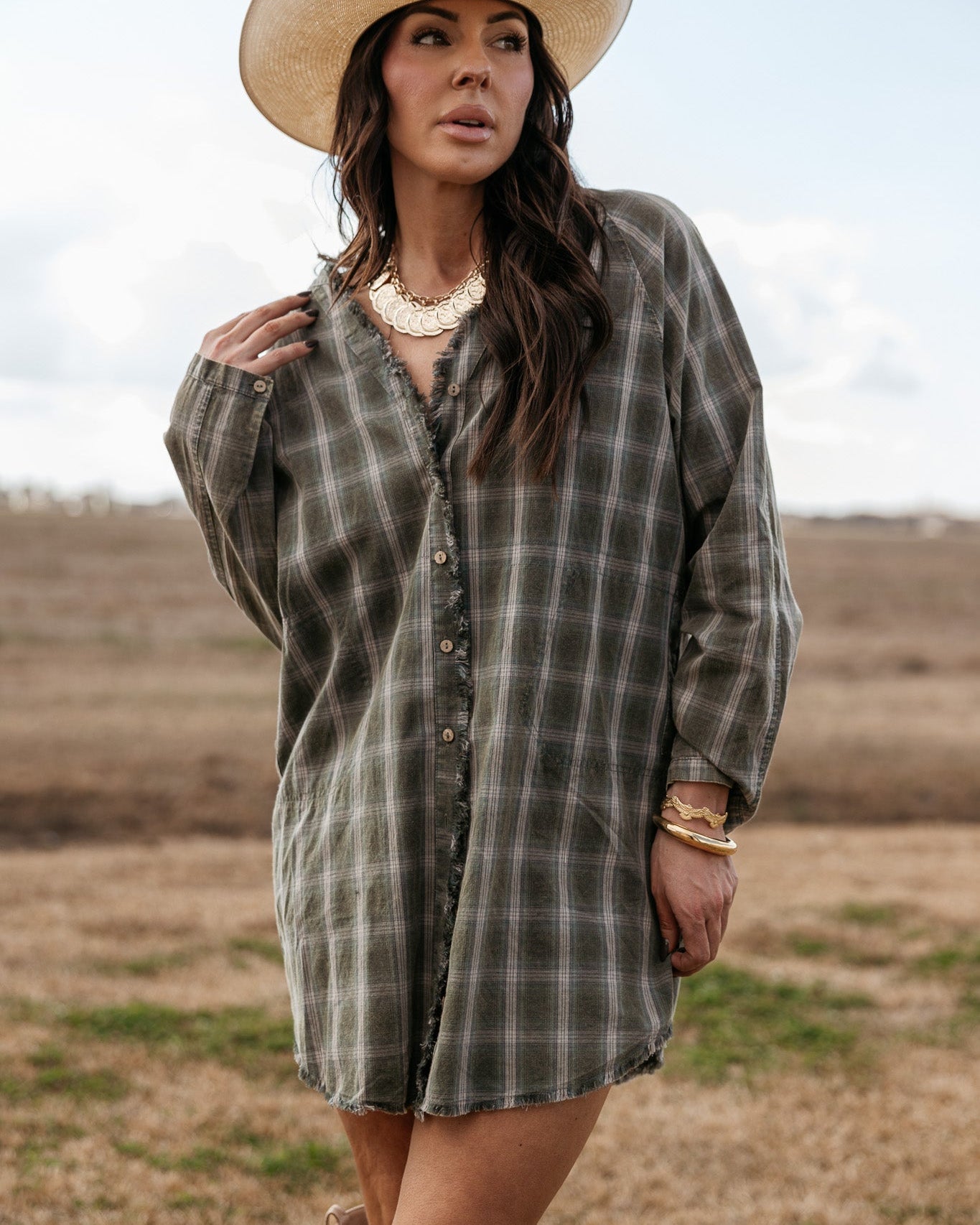 Woman in a plaid western shirt dress, cowboy hat, and statement jewelry outdoors