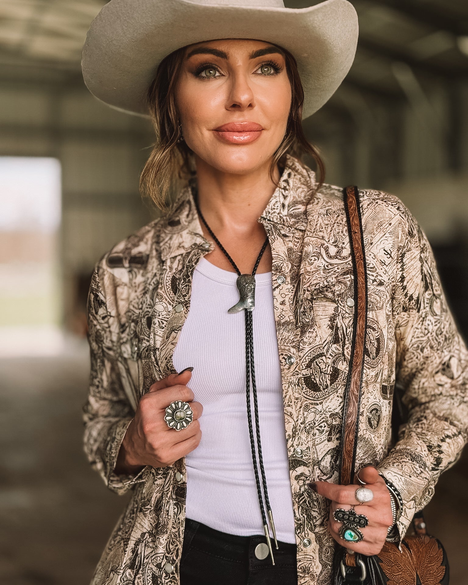 Woman in a white cowboy hat, western bolo tie, boho print shirt, and turquoise rings