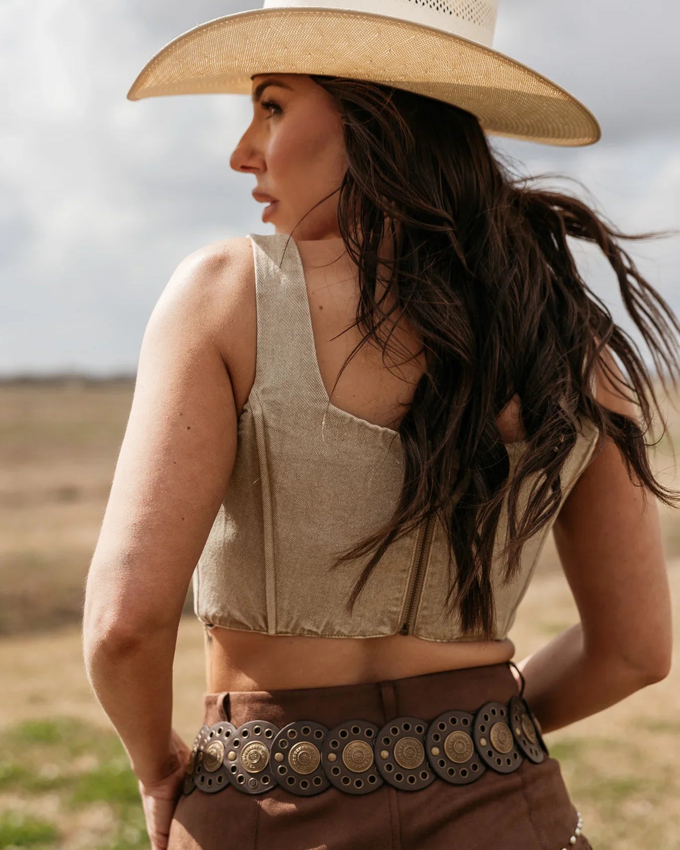 Woman wearing a cowboy hat and a patterned belt in an outdoor setting