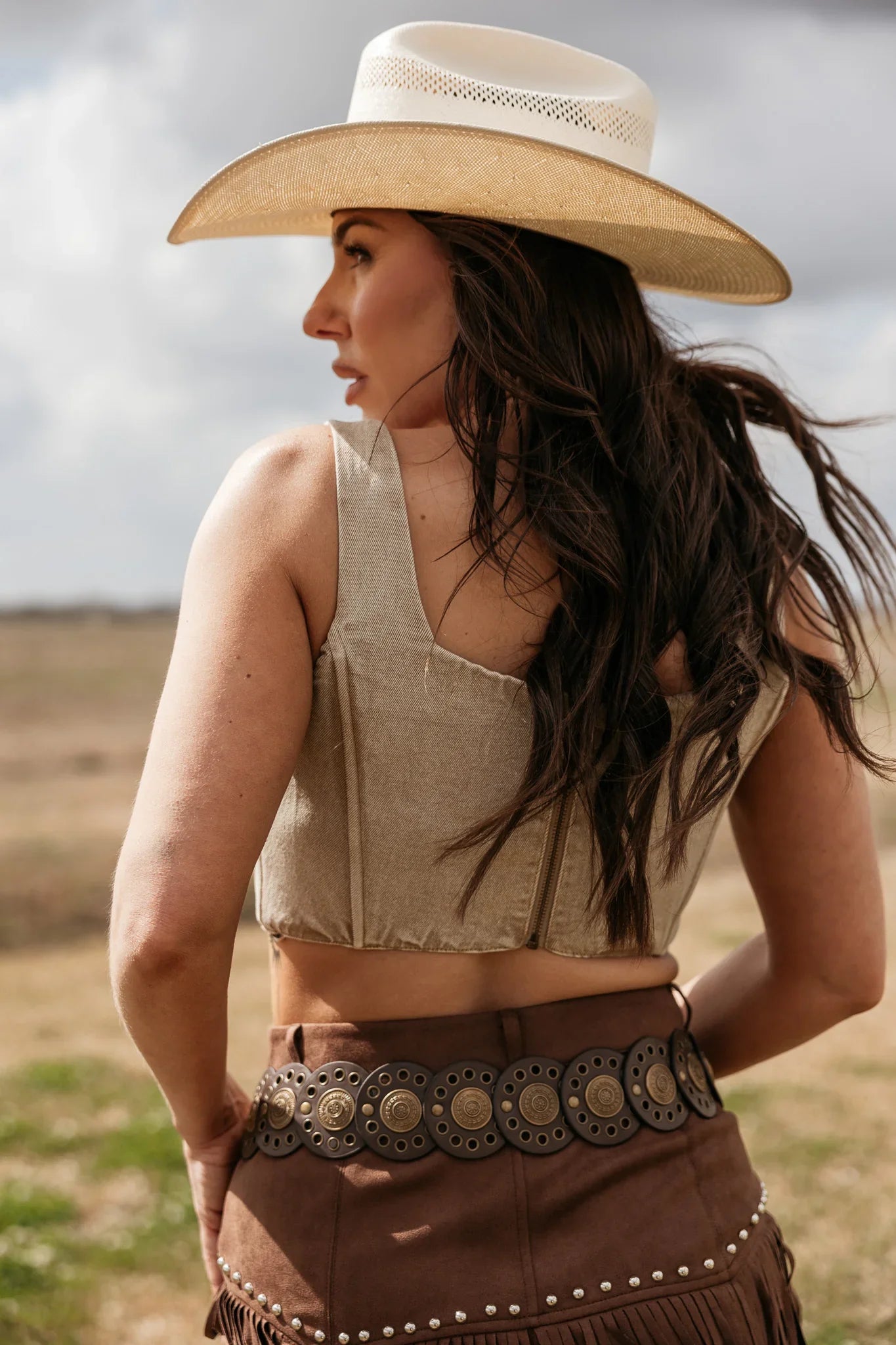 Woman wearing a cowboy hat and a patterned belt in an outdoor setting