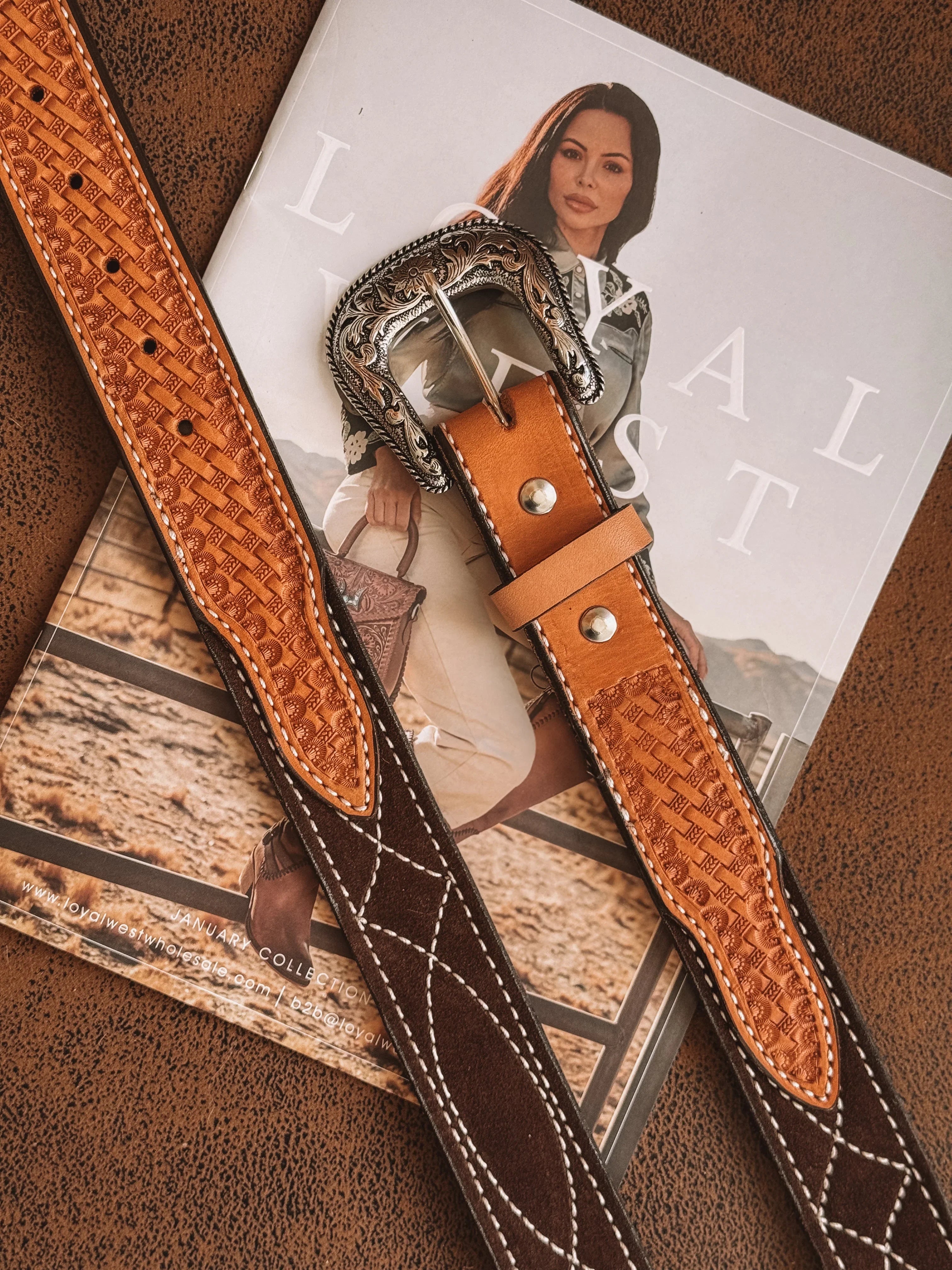 Tooled leather western belt with ornate silver buckle on a magazine featuring cowgirl fashion.
