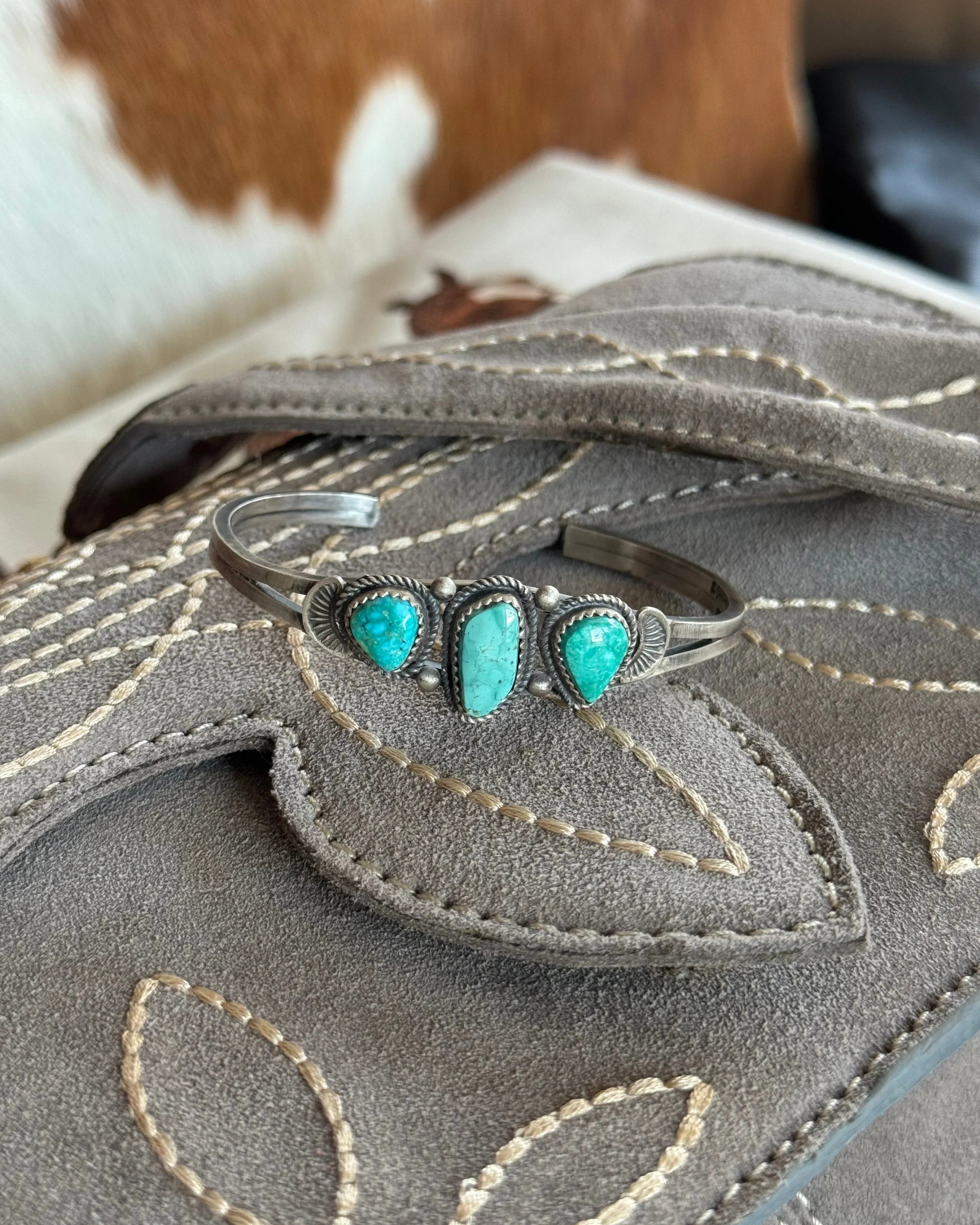 Western turquoise cuff bracelet with silver setting on embroidered suede bag, cowhide background