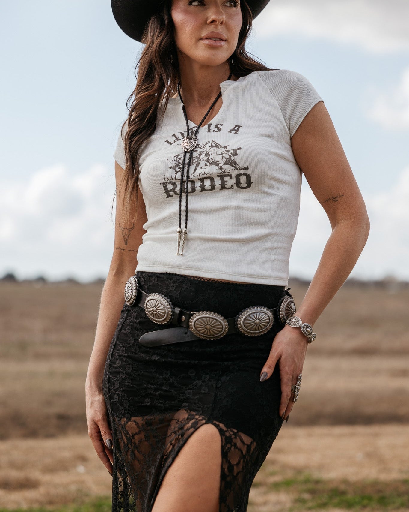 Woman in western boho outfit with cowboy hat, graphic tee, concho belt and lace skirt outdoors