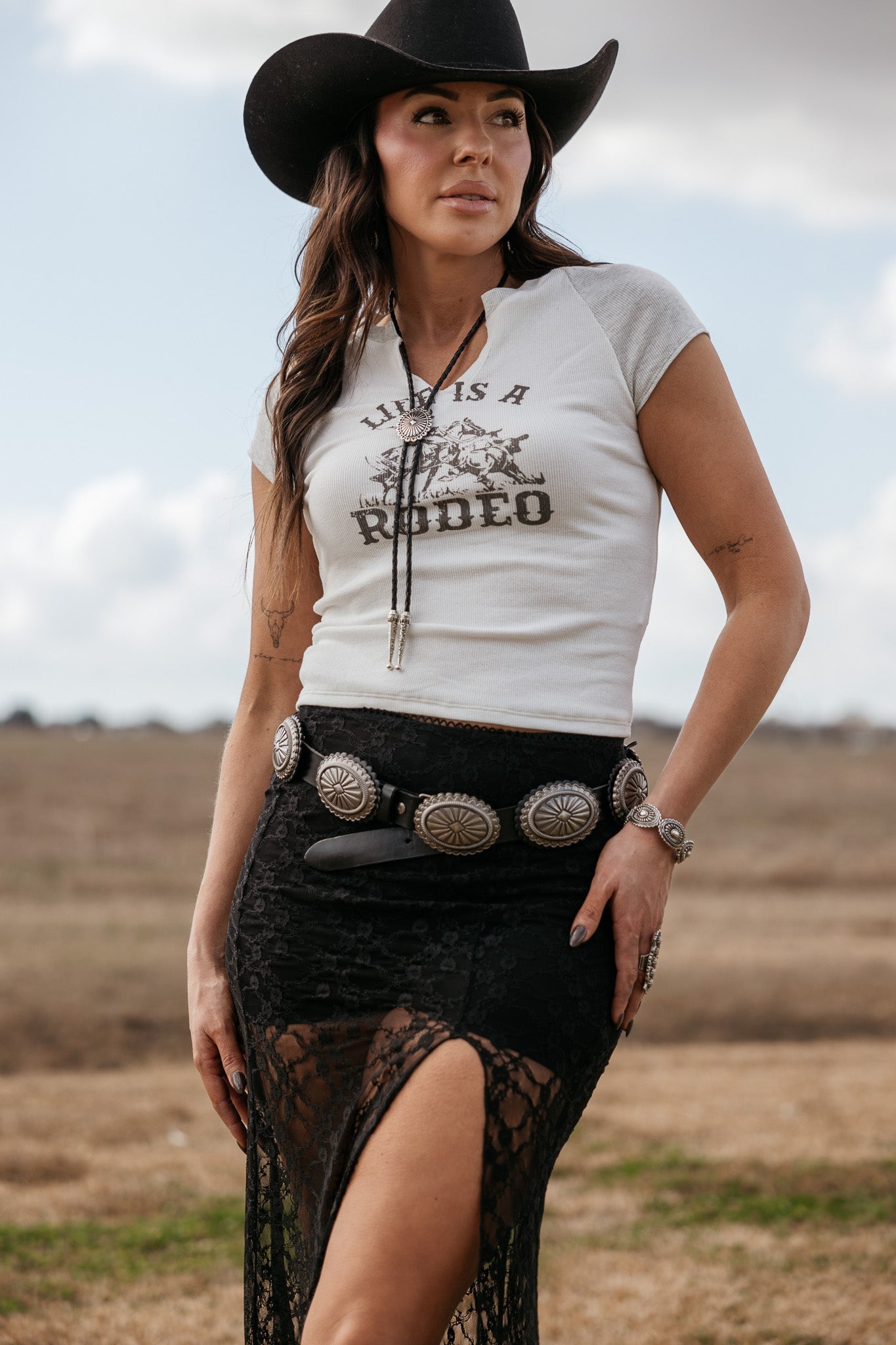 Woman in western boho outfit with cowboy hat, graphic tee, concho belt and lace skirt outdoors