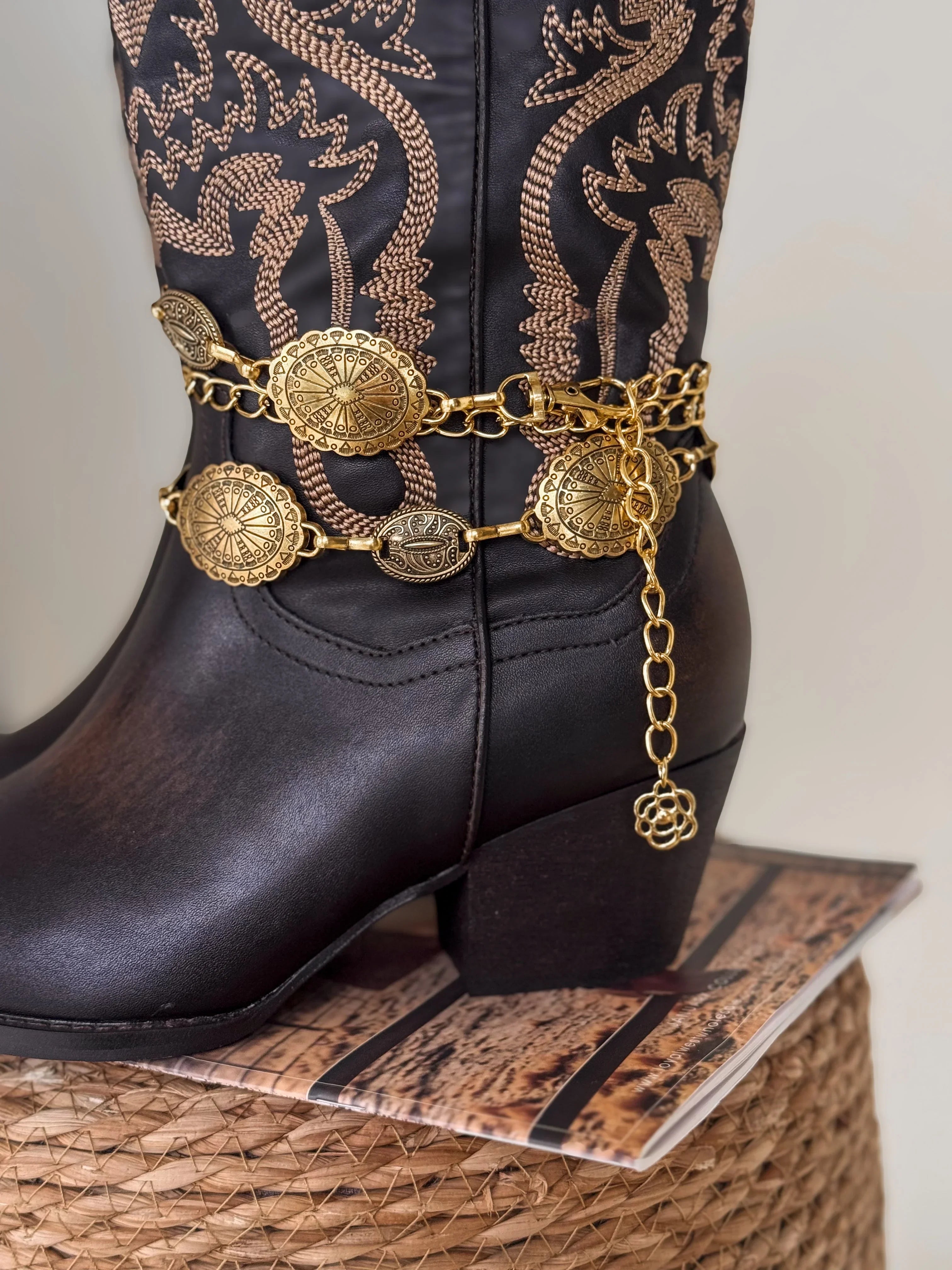 Black boot with gold chain and medallion design on a textured surface