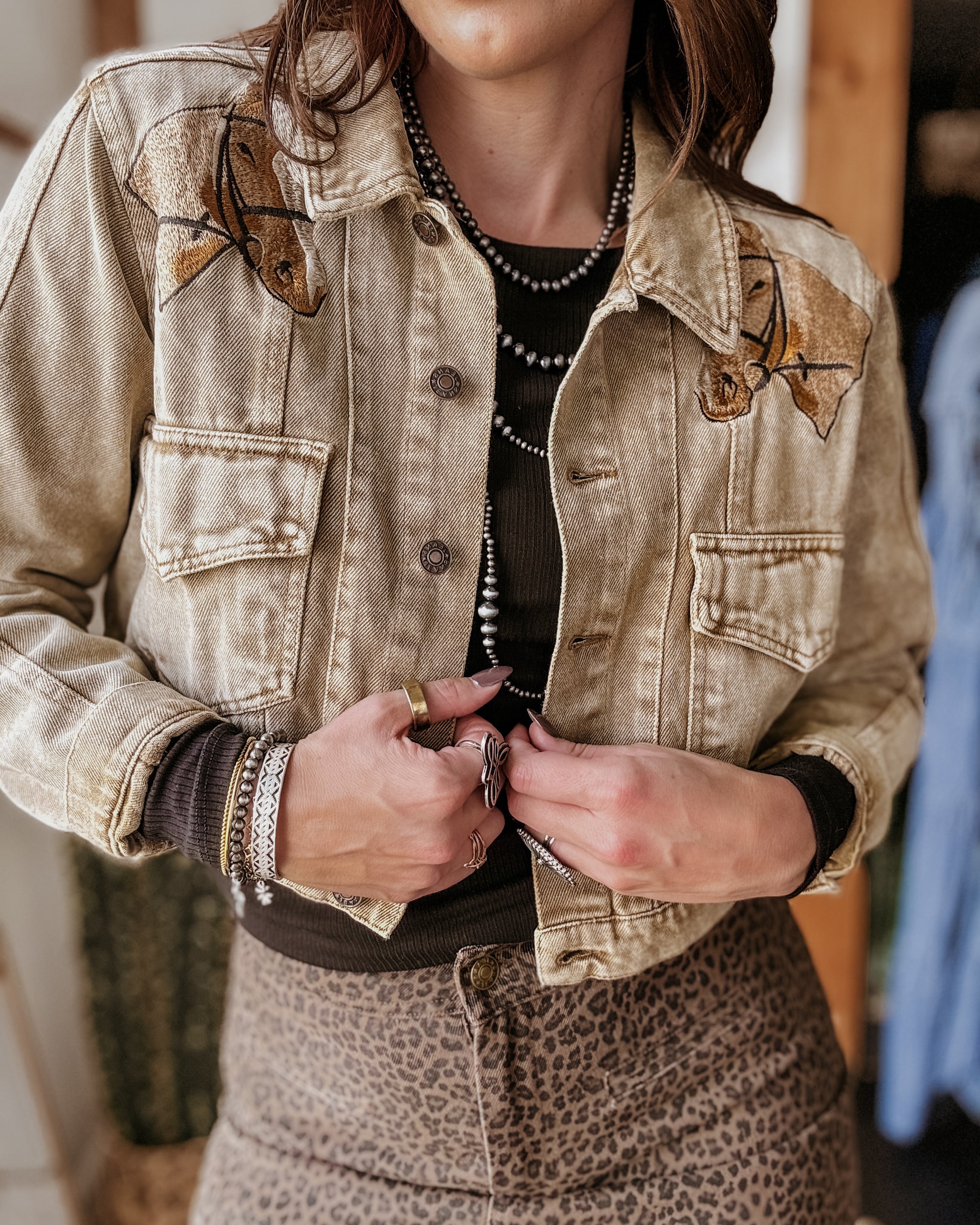 Woman wearing western embroidered denim jacket, layered jewelry, and leopard print skirt