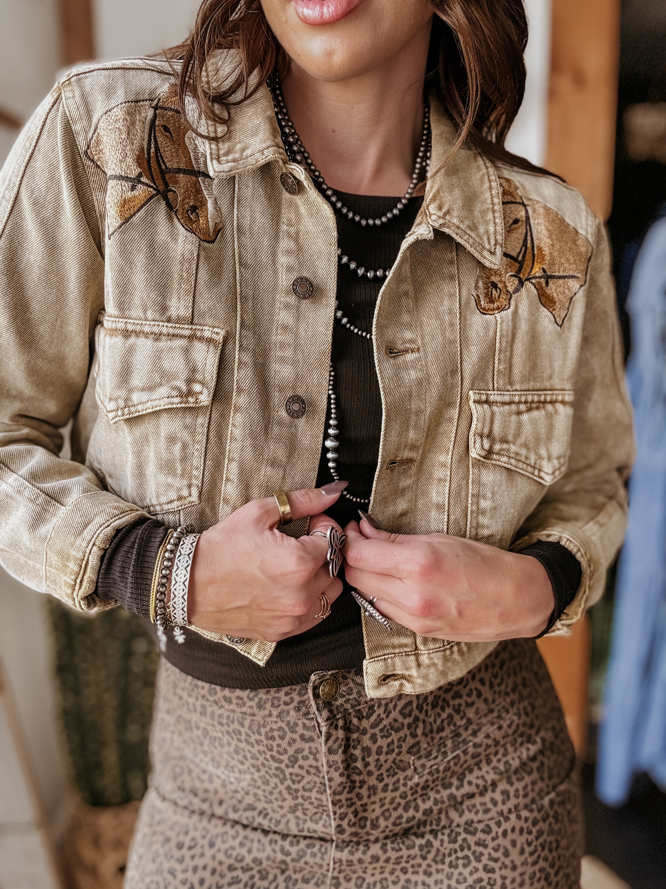 Woman wearing western embroidered denim jacket, layered jewelry, and leopard print skirt