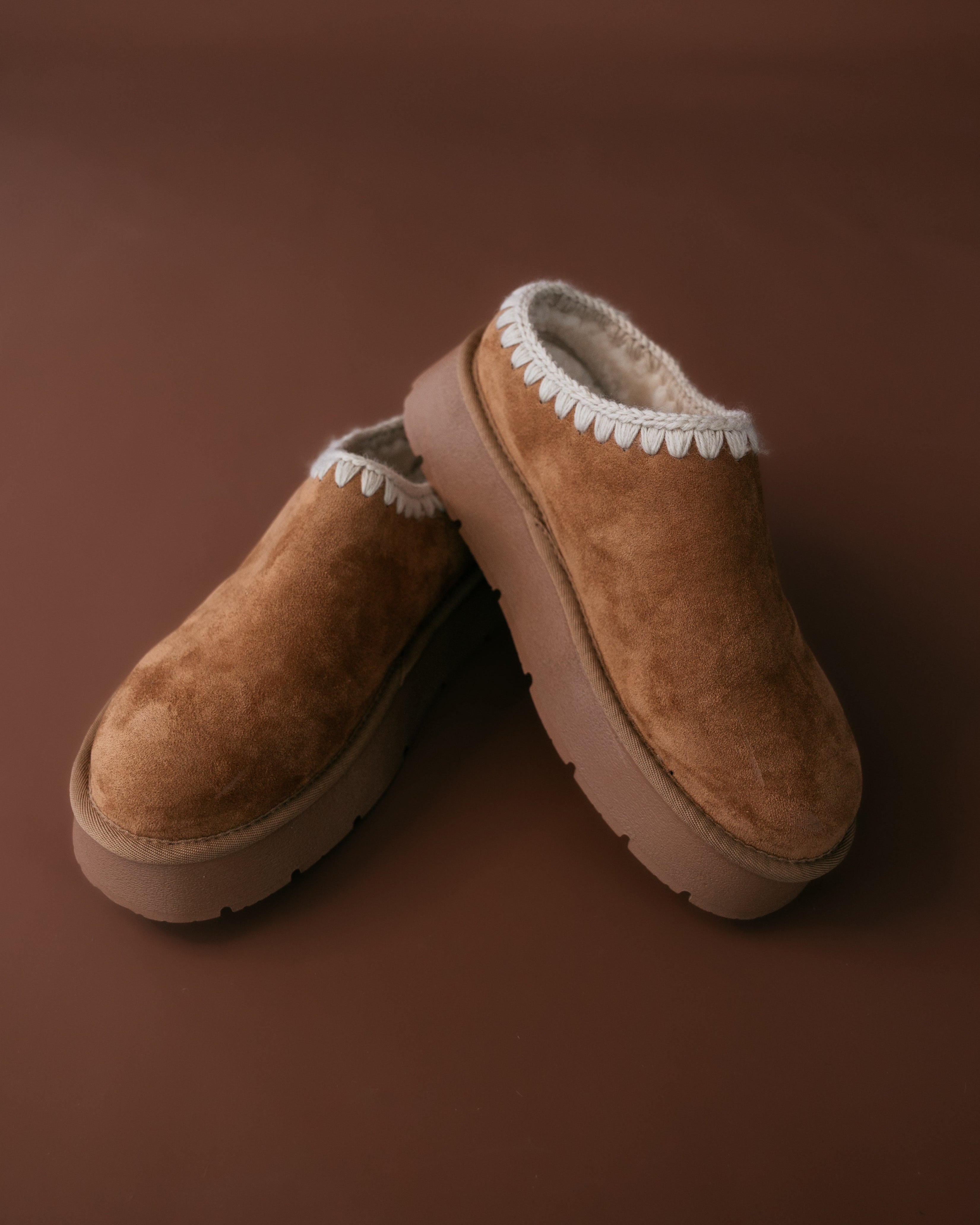 Pair of brown slippers with white fur lining on a brown background