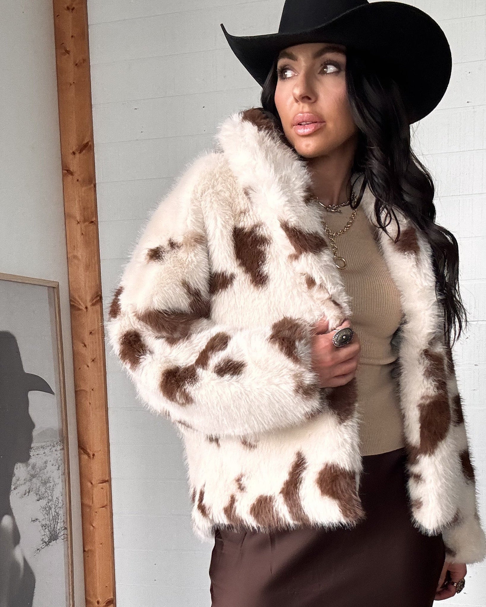 Woman wearing a cow print fur coat and black hat indoors.