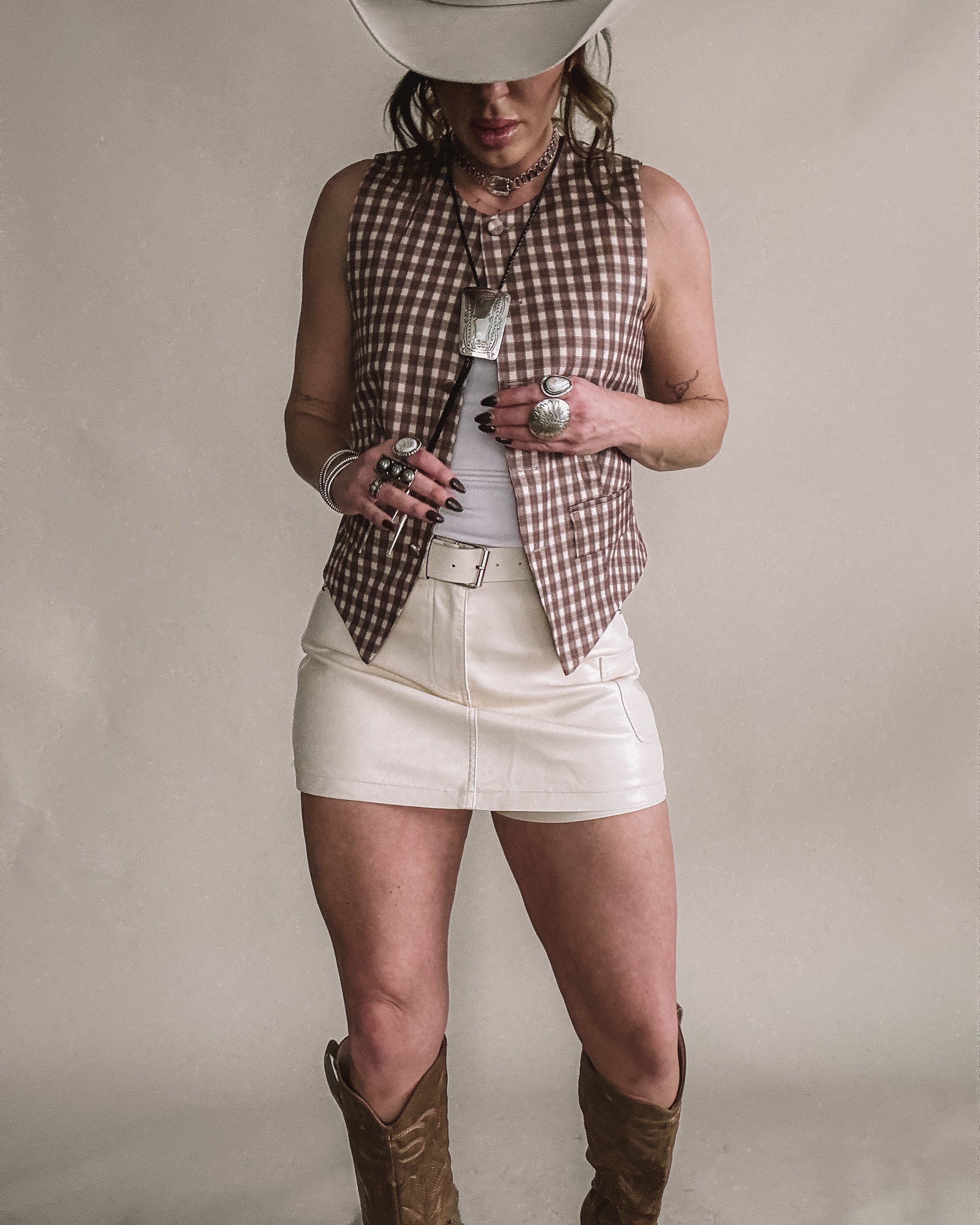 Woman in cowgirl hat wearing western vest, white mini skirt, cowboy boots, and boho jewelry