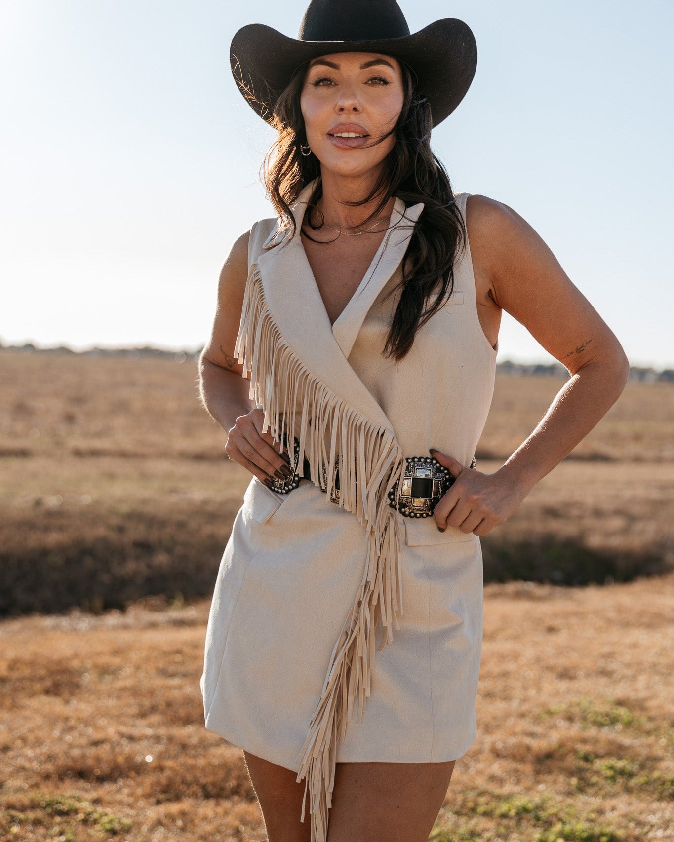 Woman in cowgirl hat and fringed western dress with concho belt standing outdoors