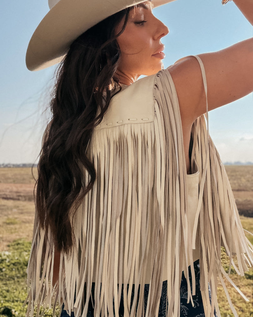 Woman in cream fringe vest and cowboy hat, western boho style, outdoor setting
