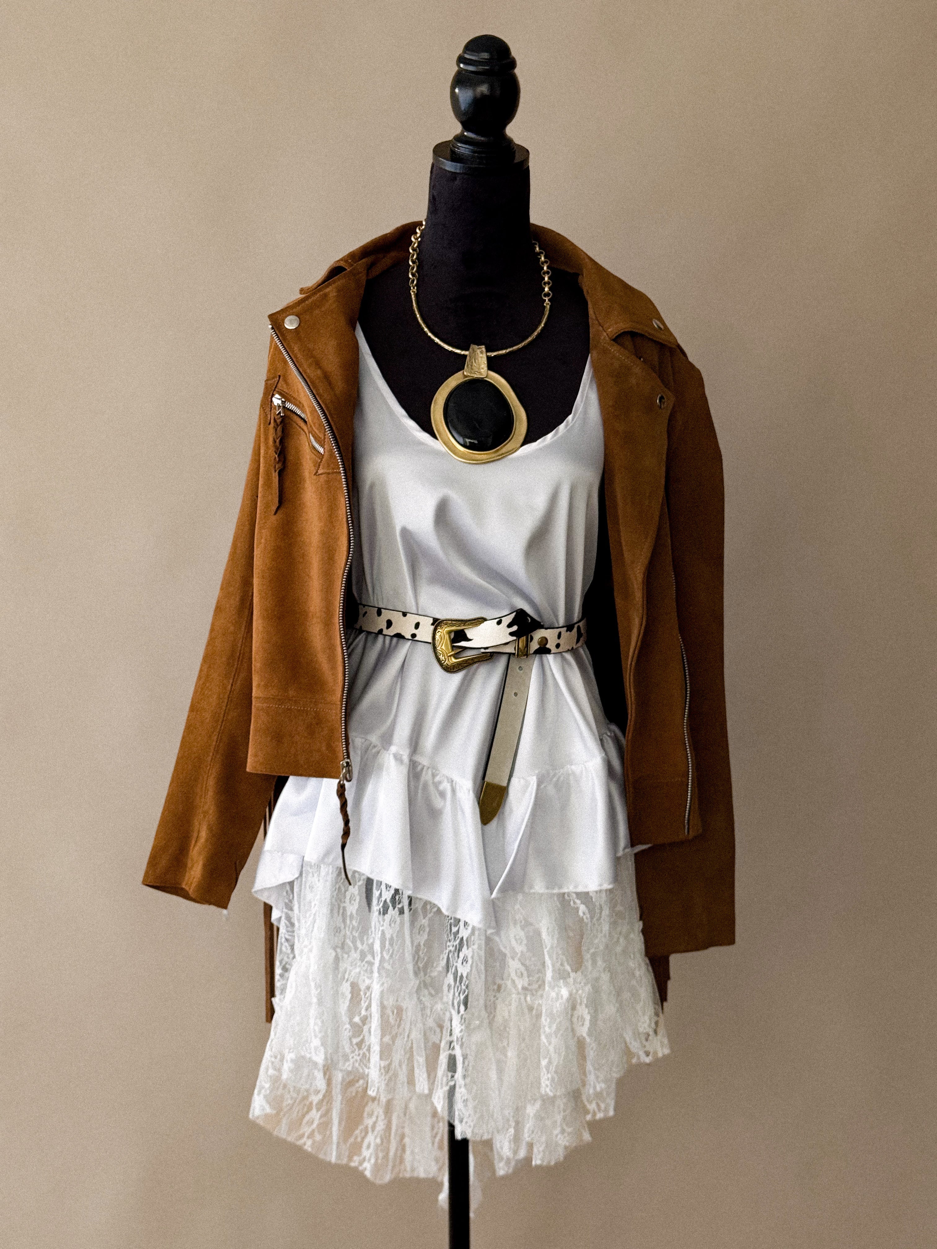 Mannequin wearing a white lace ruffle dress, tan suede jacket, statement necklace, and western belt