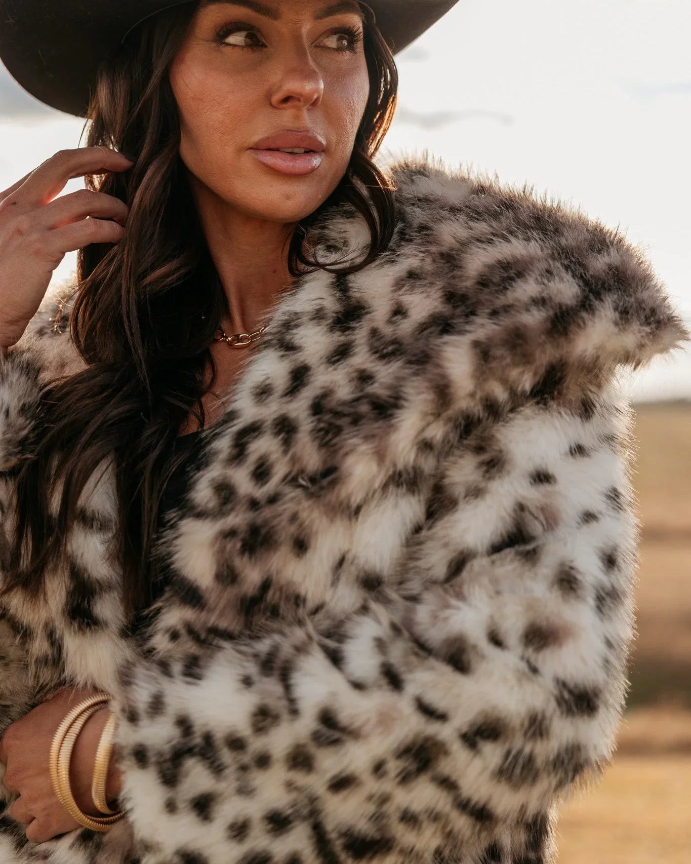 Woman in black cowboy hat and faux fur leopard print coat outdoors, western boho fashion