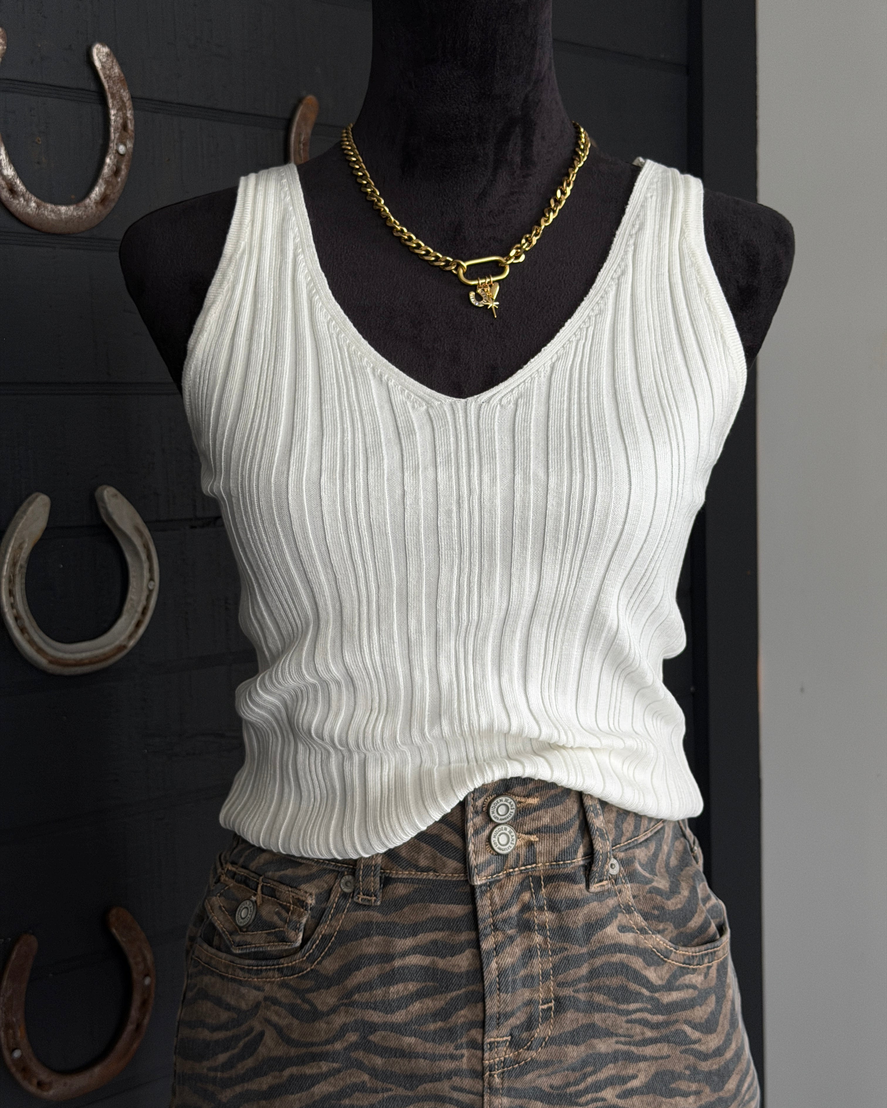 Mannequin wearing a white ribbed tank top and zebra print pants with a gold necklace against a dark background.